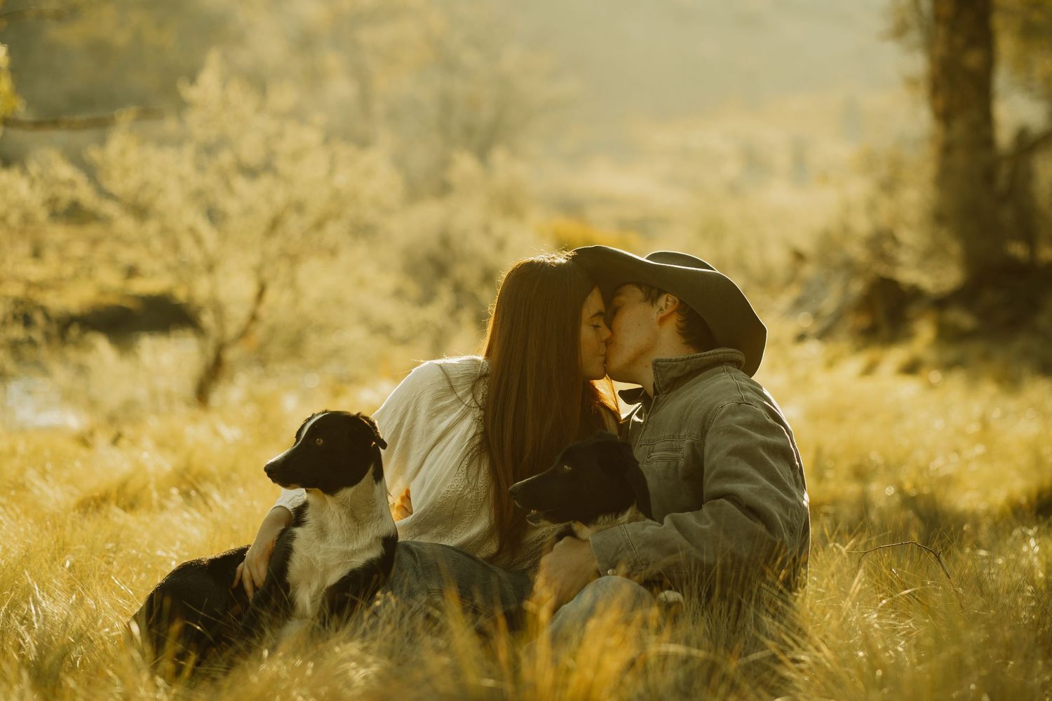 A romantic couple shares tender moment in golden field with dog sitting nearby.