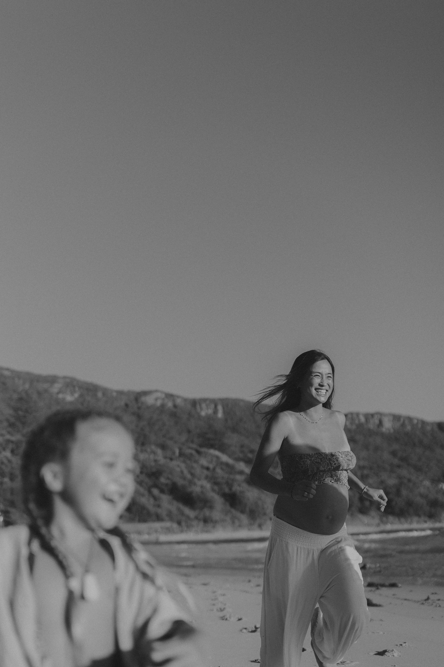 A black and white photo series shows a person moving gracefully on a beach with mountains in the distance.