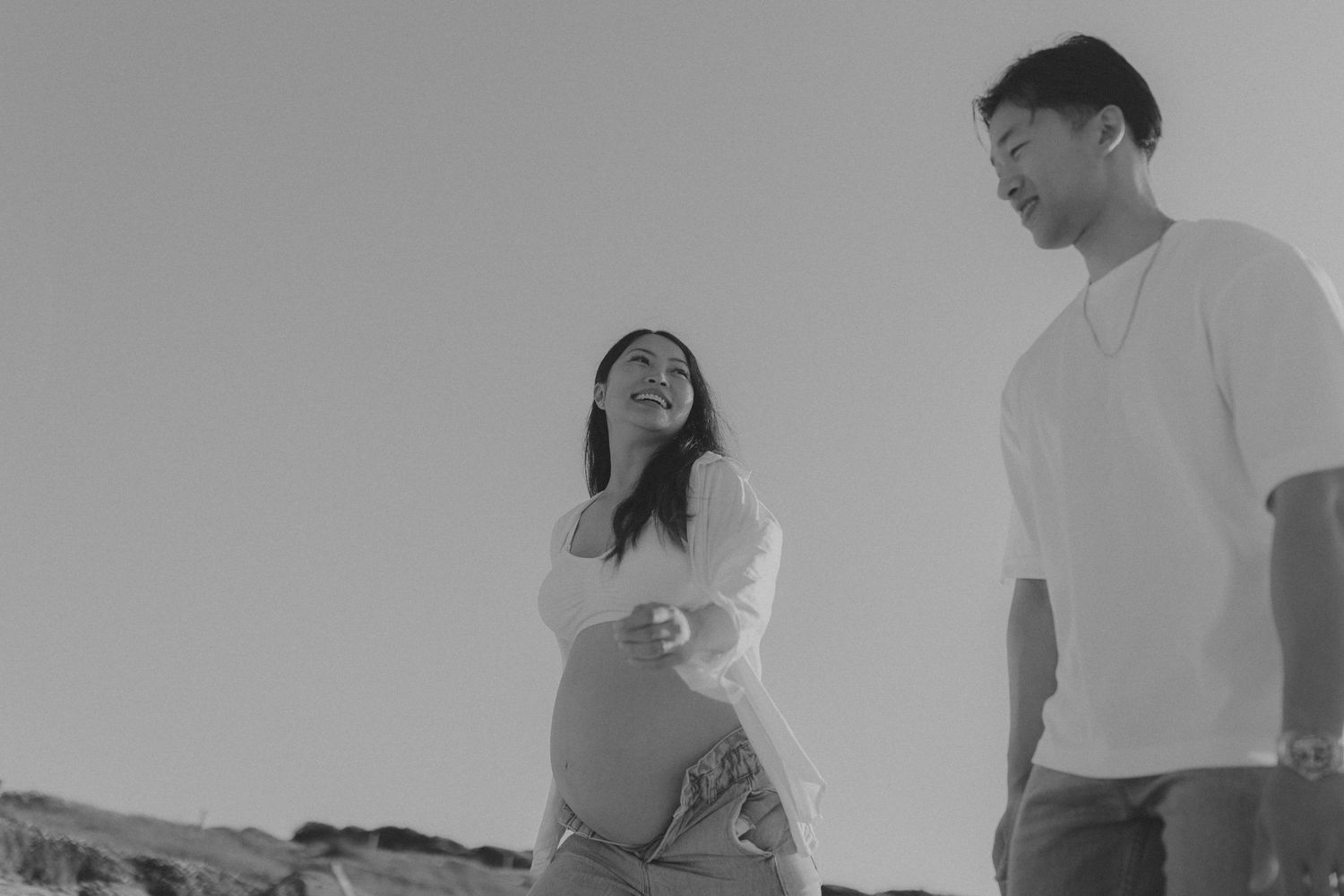 Black and white portrait of couple in casual attire against neutral background.