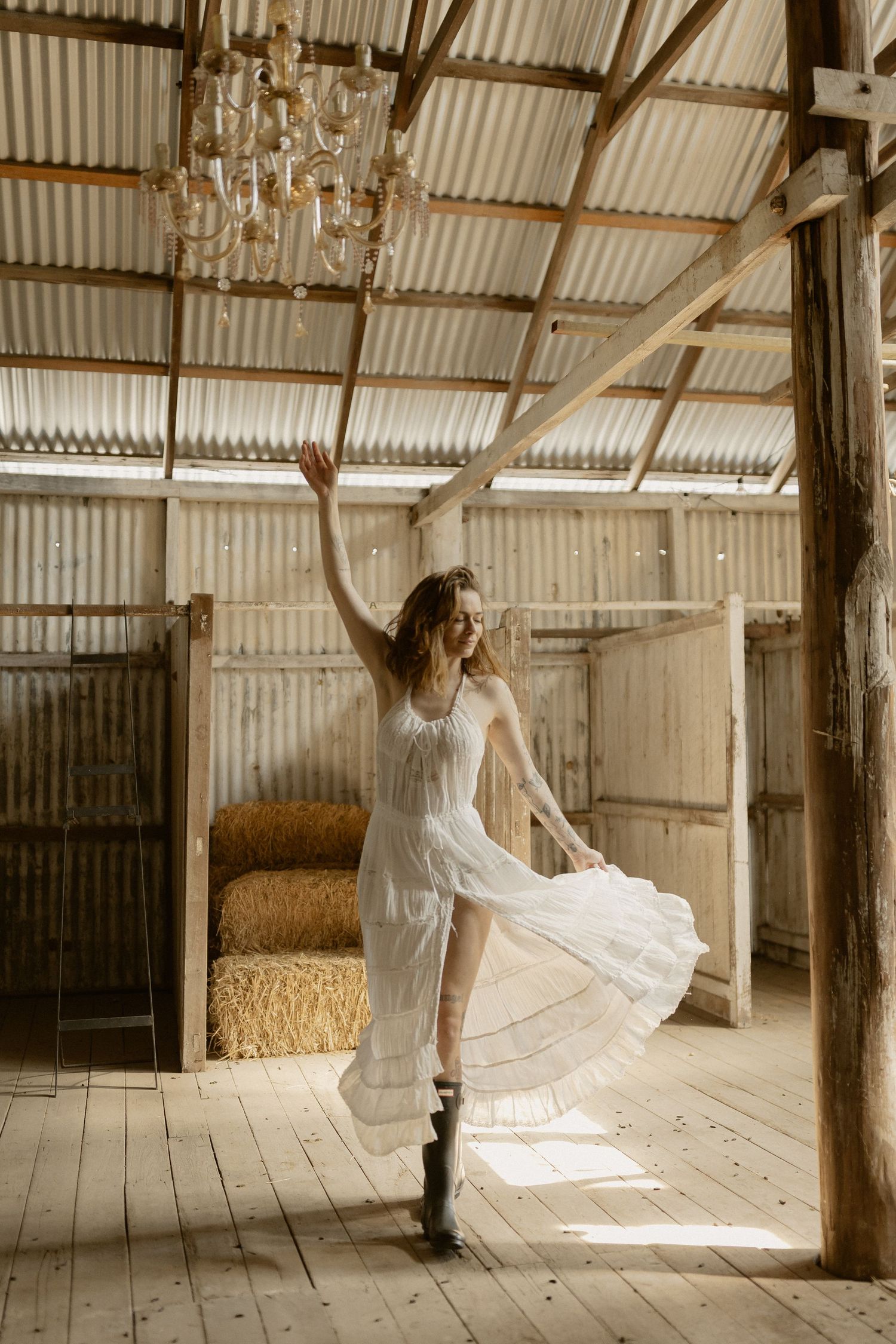 A flowing white dress twirls gracefully inside a rustic barn with sunlight streaming through.