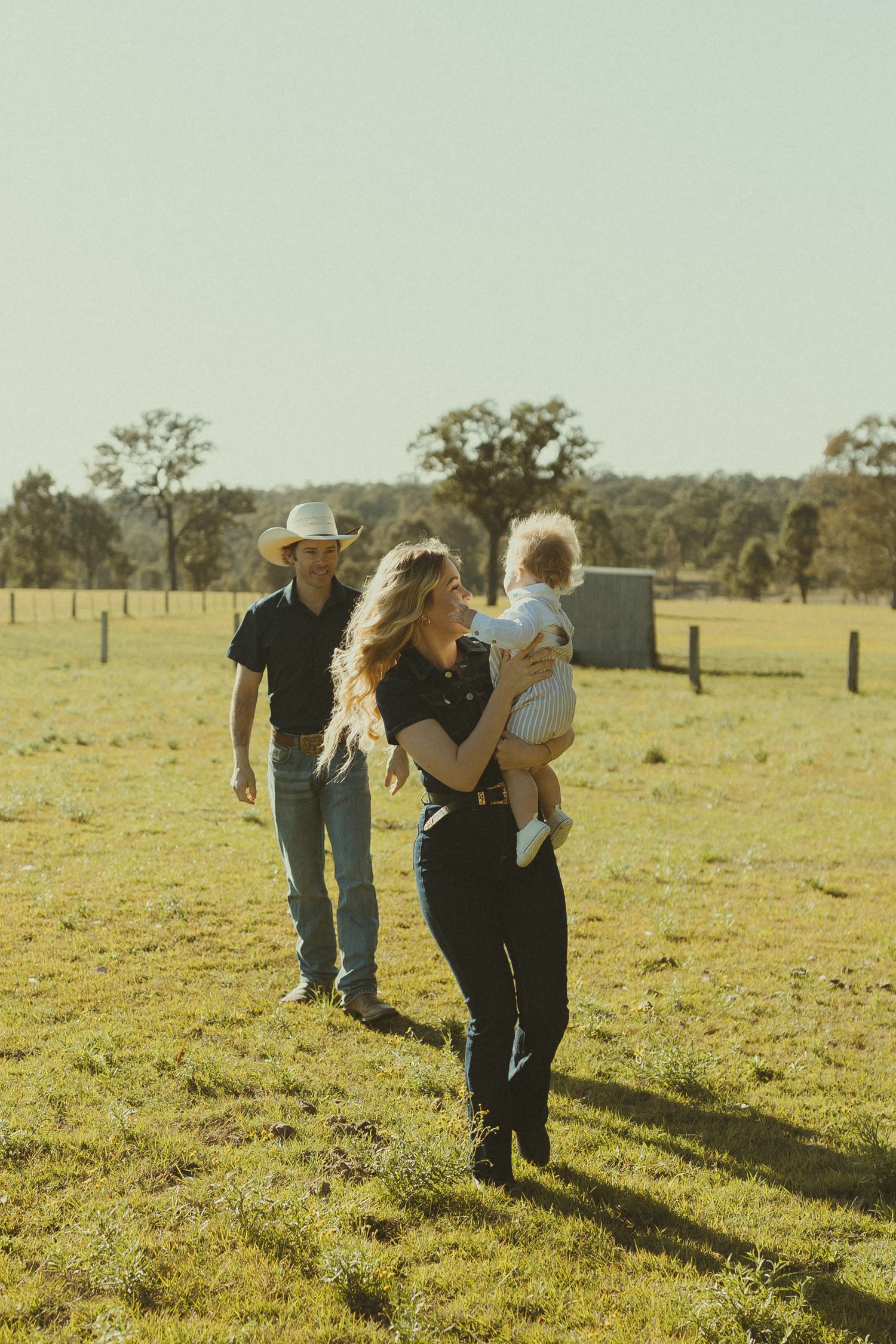 People walking together across a sunlit rural pasture with trees in the background.
