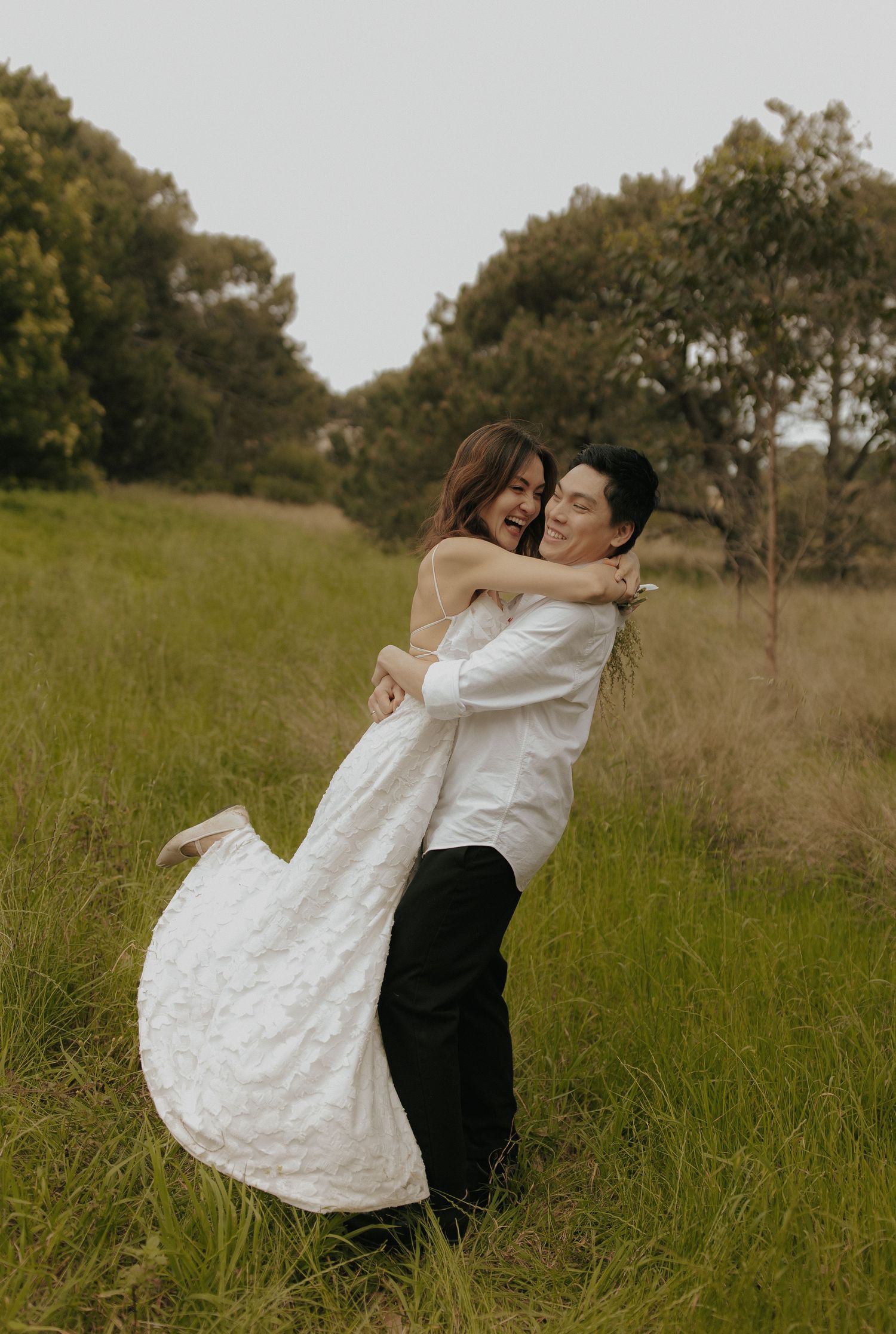 A couple spins together joyfully in a meadow of tall grass during their wedding shoot.