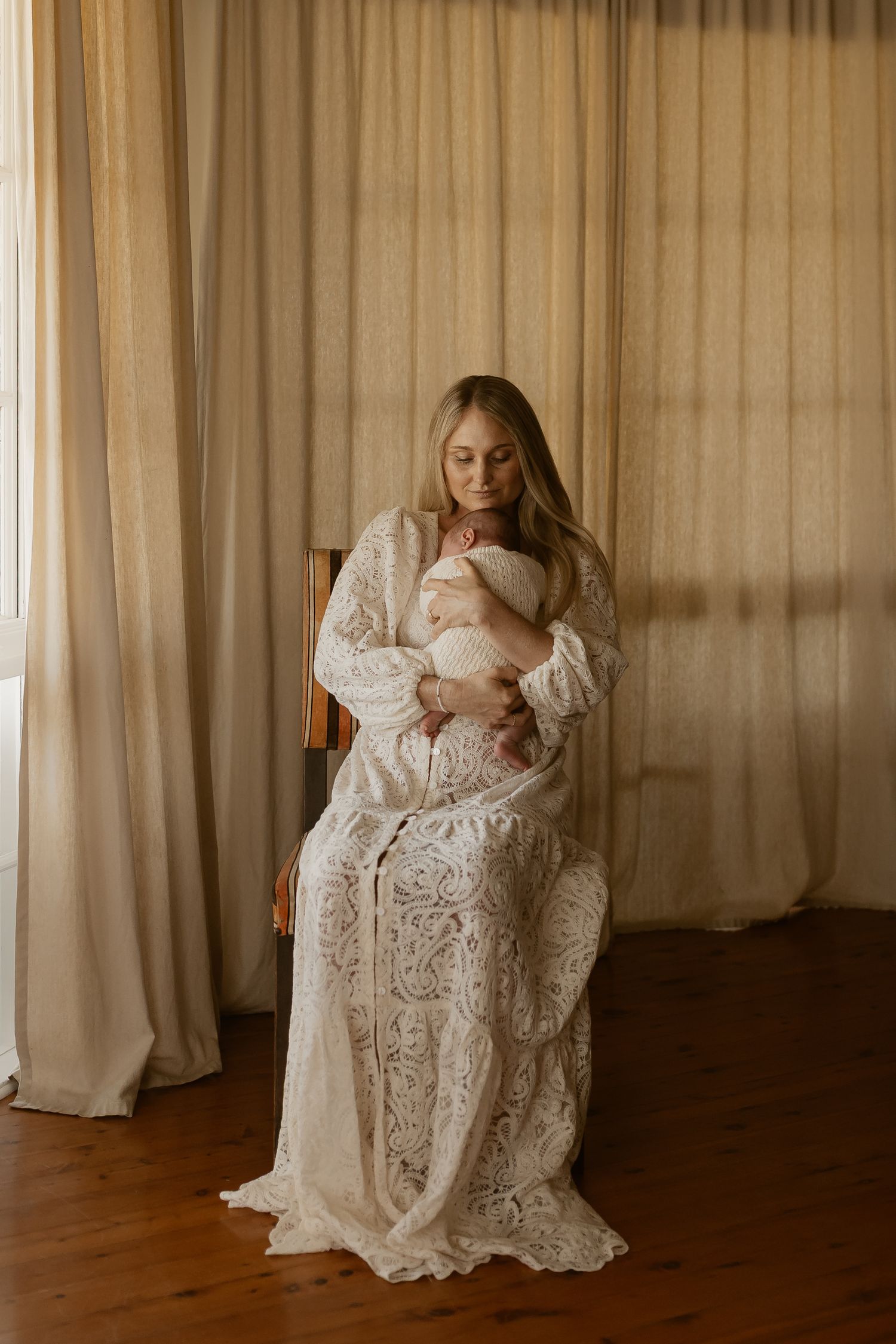 A mother in a vintage white lace dress sits in a moody room holding a baby across multiple artistic photographs.