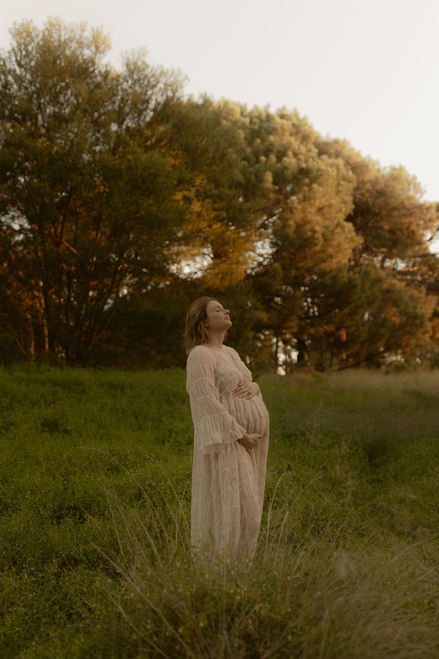 Ethereal maternity portraits in flowing white dresses against a sunset-lit natural backdrop.
