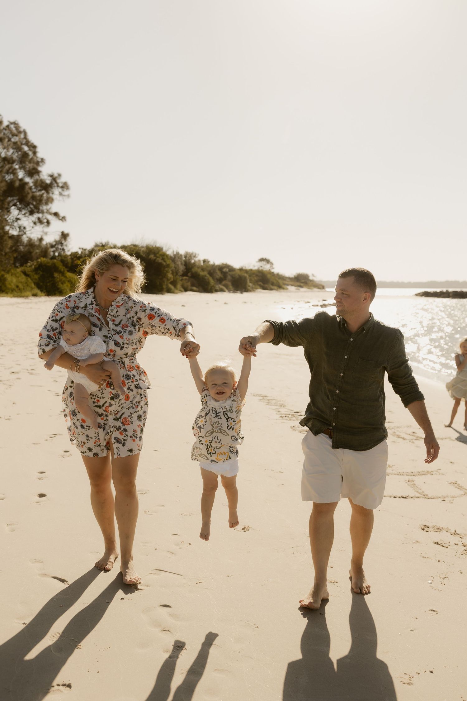 Parents swinging child between them while walking on sunny beach.