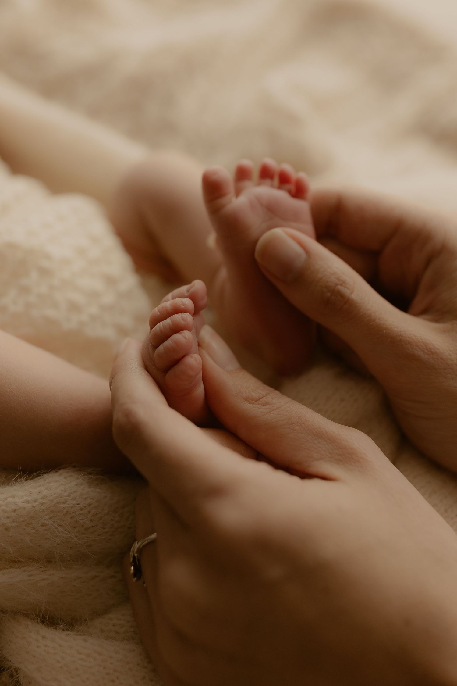 Gentle hands tenderly holding tiny newborn feet wrapped in soft blanket.