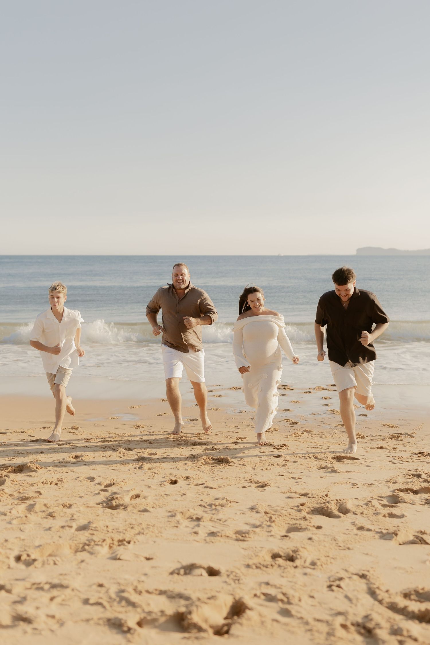A group of people playfully running and jumping together on a sandy beach by the ocean.
