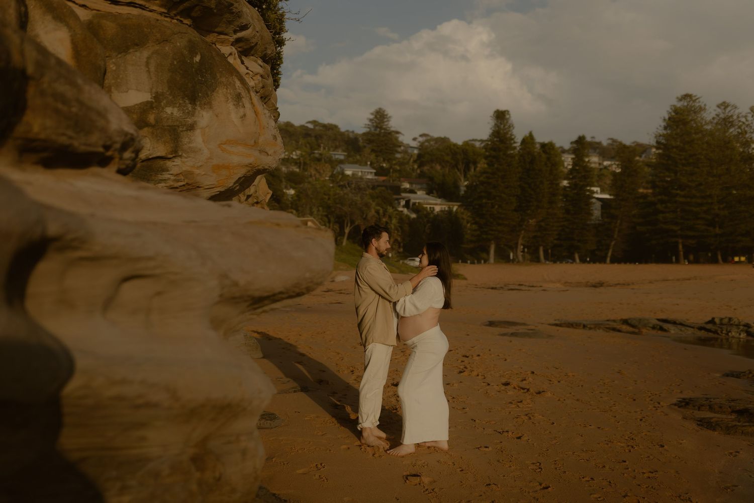 A couple walks along a scenic beach path during sunset with dramatic cliffs and ocean views in the background.