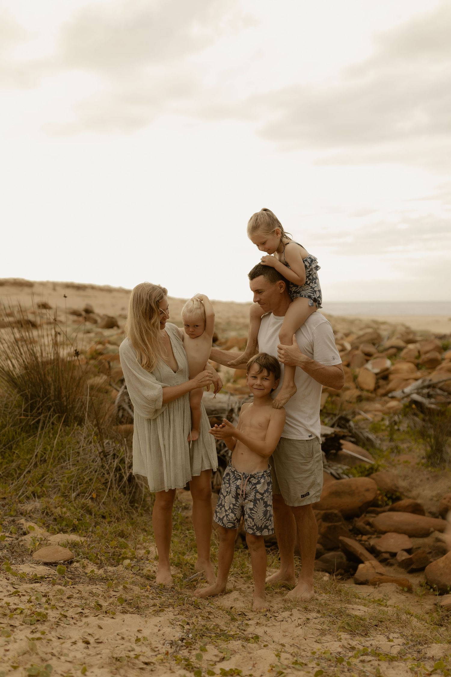 A family plays together on a rocky beach during a cloudy afternoon.