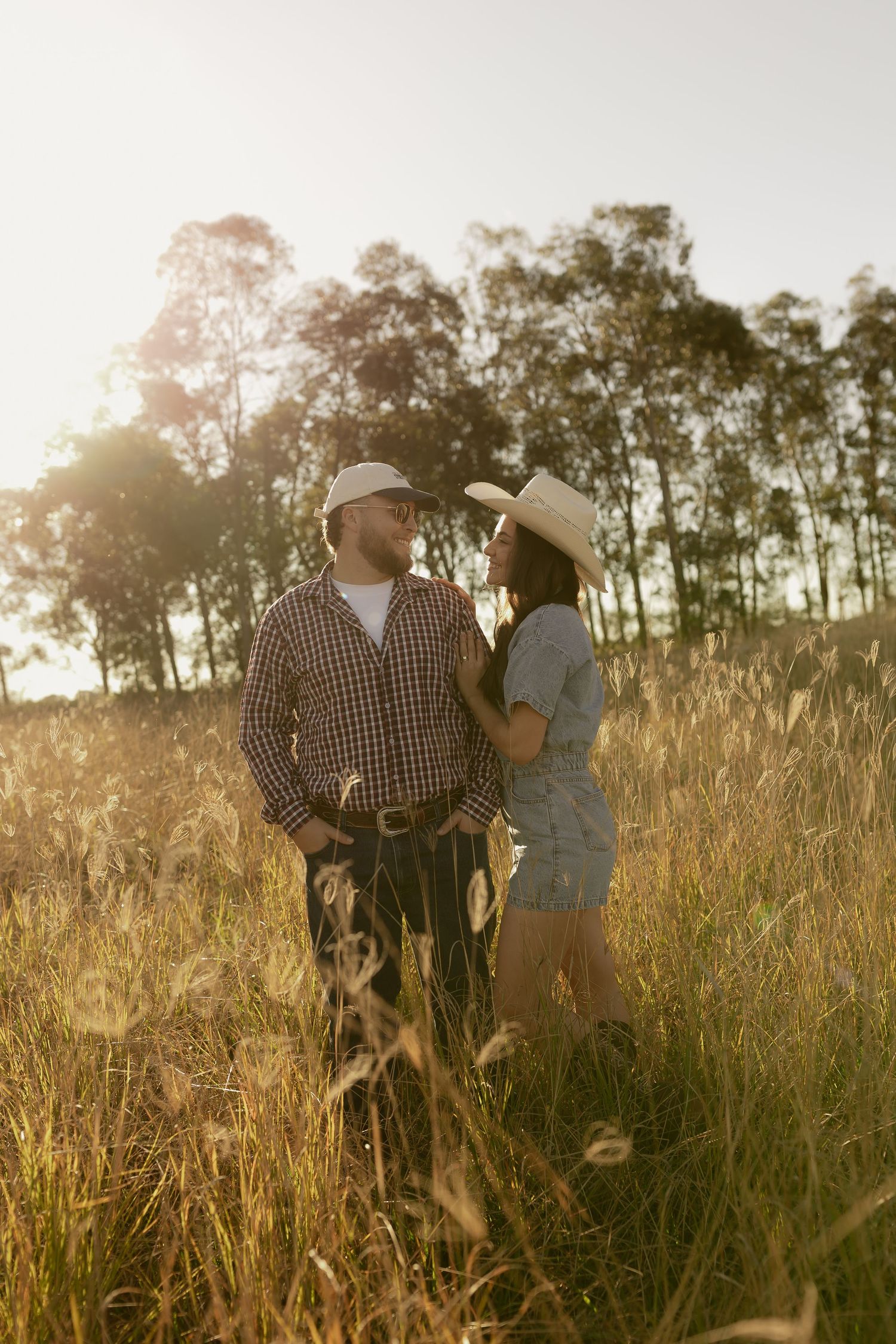 Couple in cowboy hats sharing a romantic moment in a golden sunlit field with trees in the background.