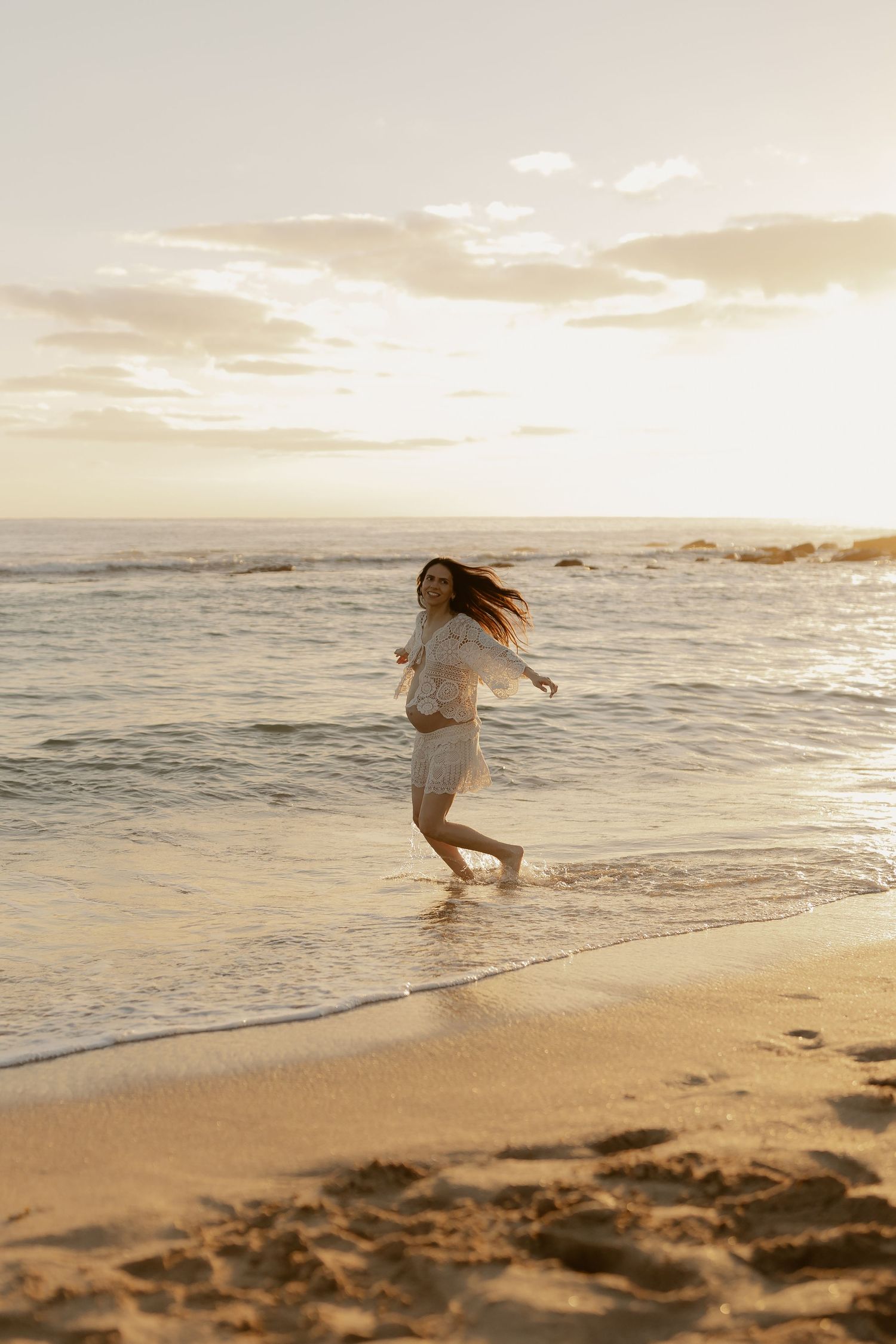A person in white dress playfully splashes in the ocean waves during golden hour on a tropical beach.