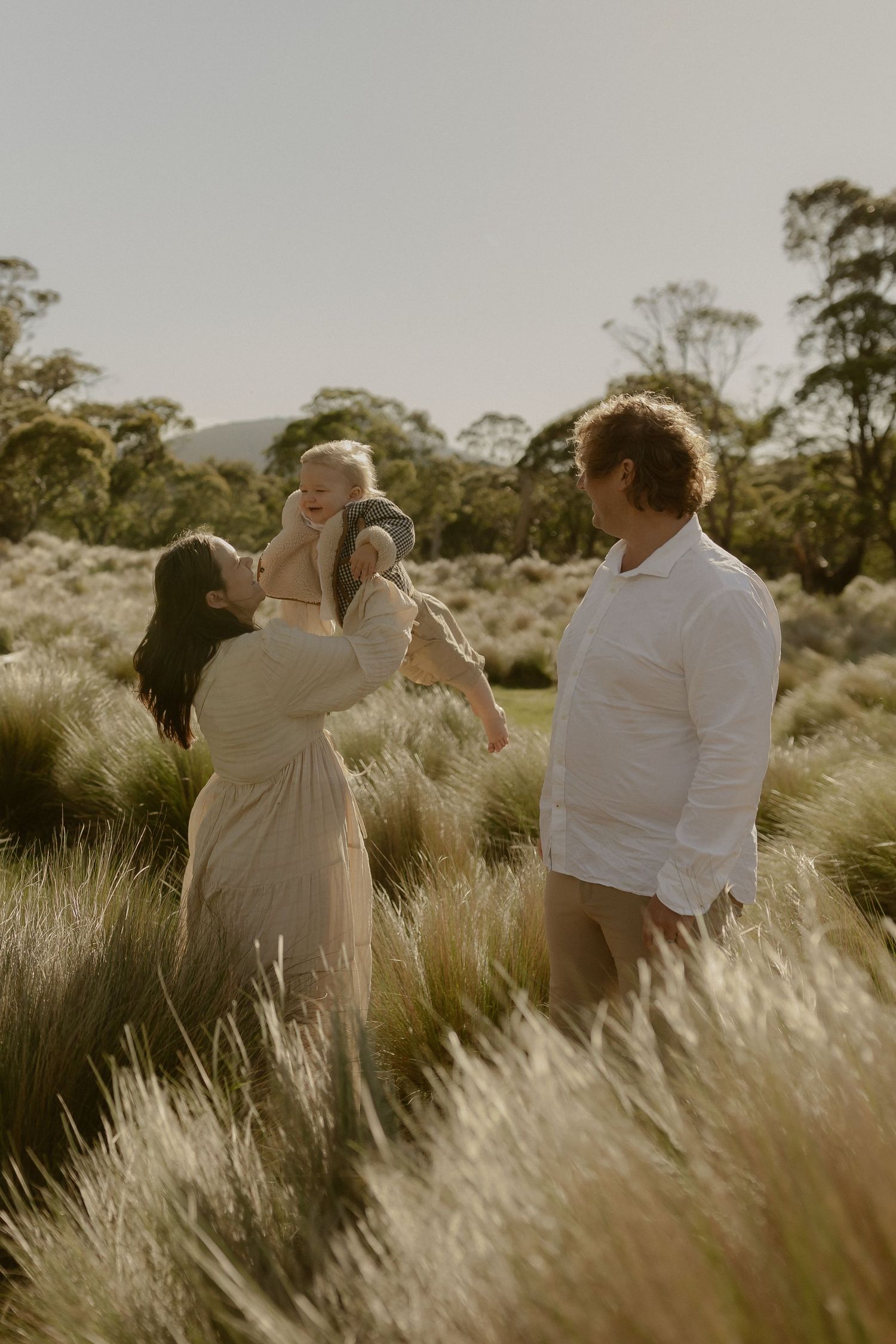 Couple embraces romantically in golden sunlit field of tall grass during sunset.