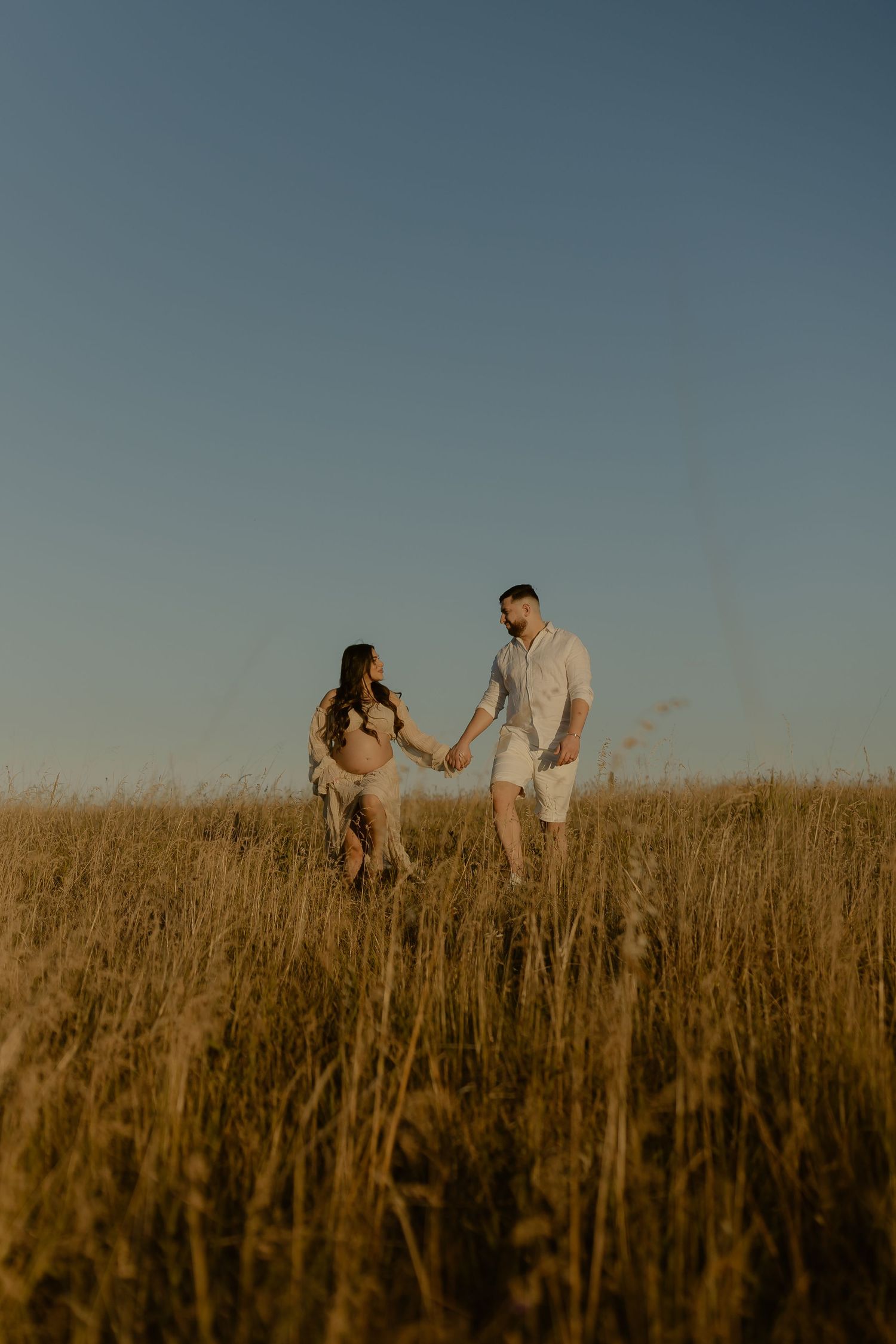 Romantic couple dances and spins together in tall grass field at dusk.