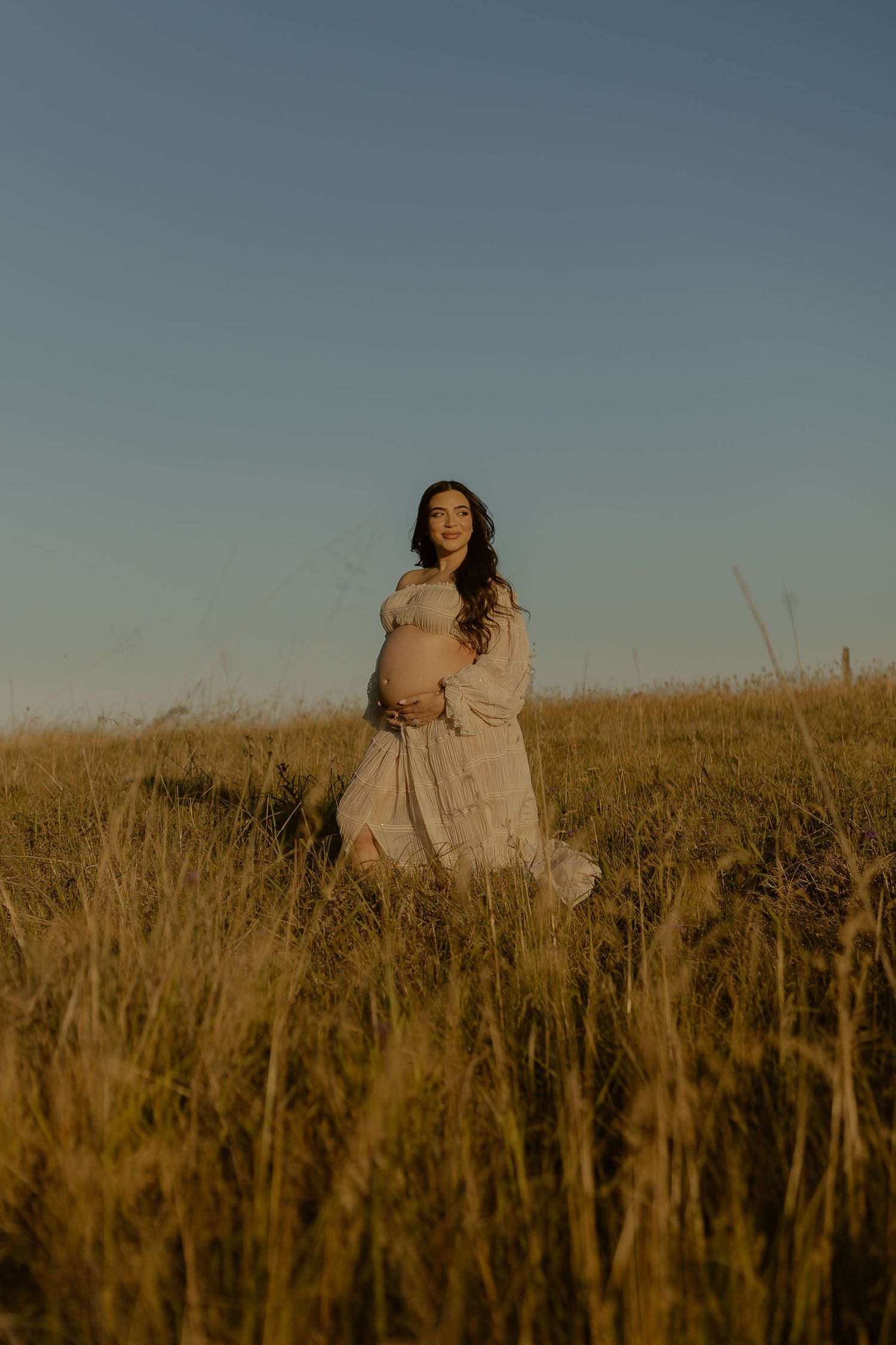 A person in a flowing dress stands in a golden field at sunset, creating a dreamy silhouette against the dusky sky.