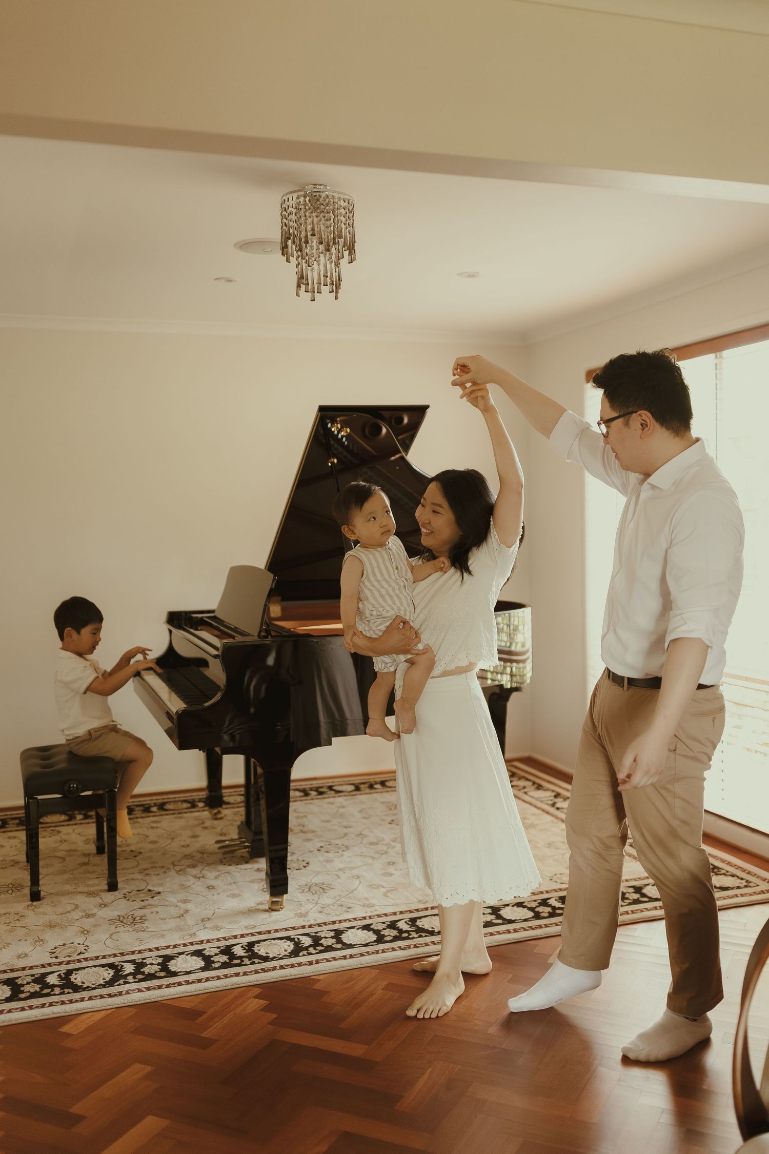 A family dances together in a bright room with hardwood floors and a piano.