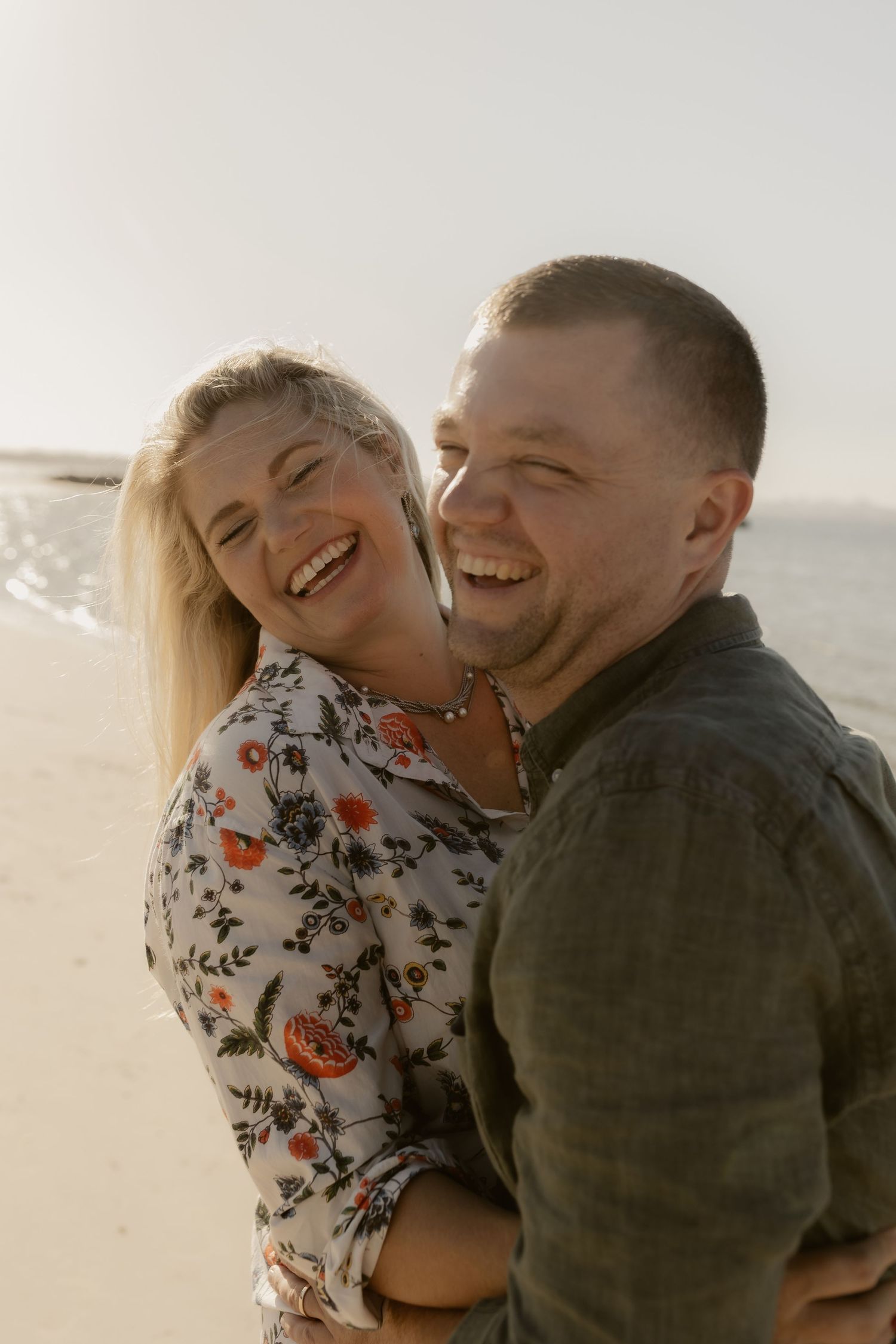 A joyful couple shares a candid laughing moment together on the beach at sunset.