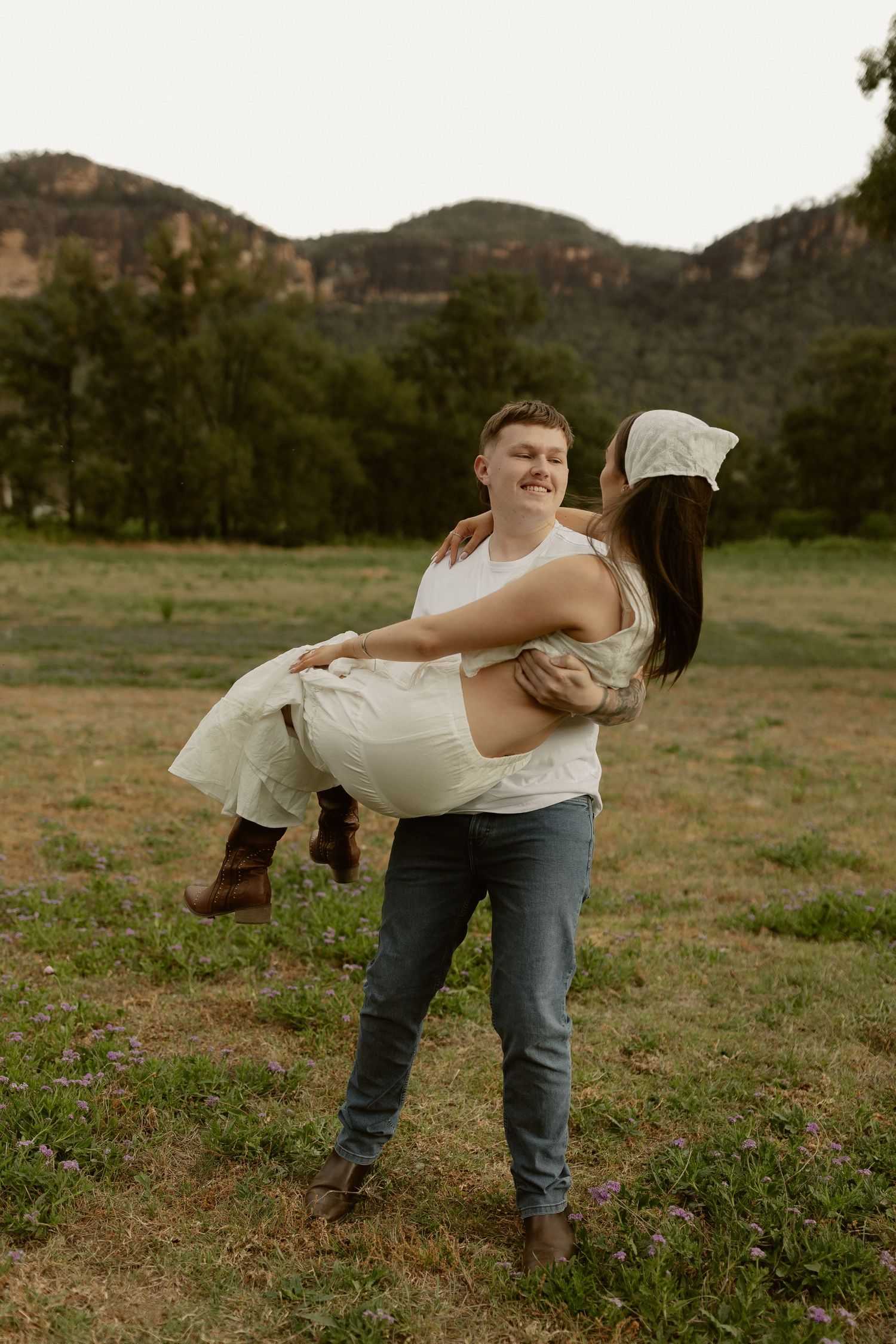 A couple embraces in a romantic dip pose against a scenic mountain landscape at sunset.
