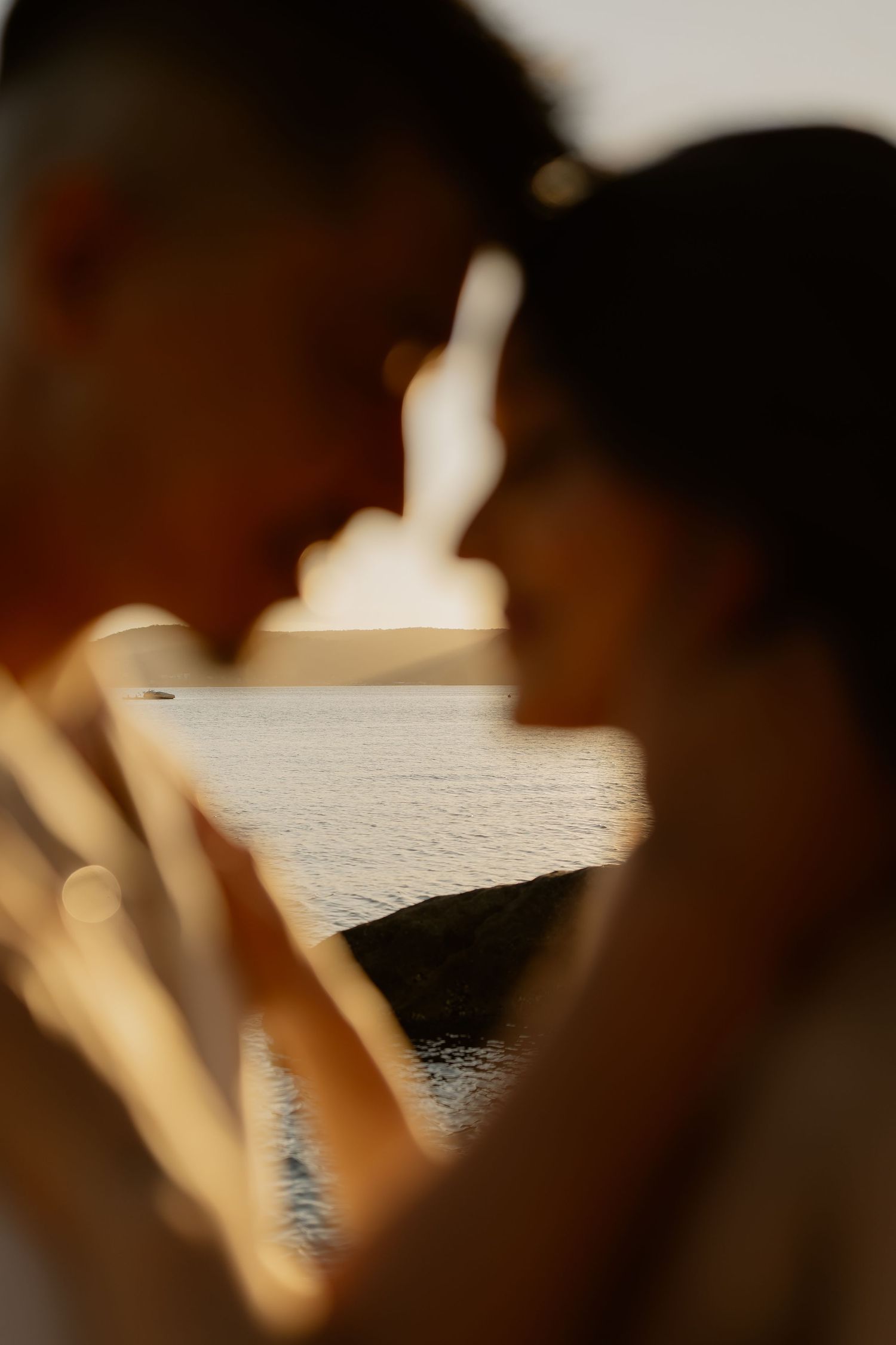 Silhouetted figures embrace against a bright ocean backdrop during golden hour.