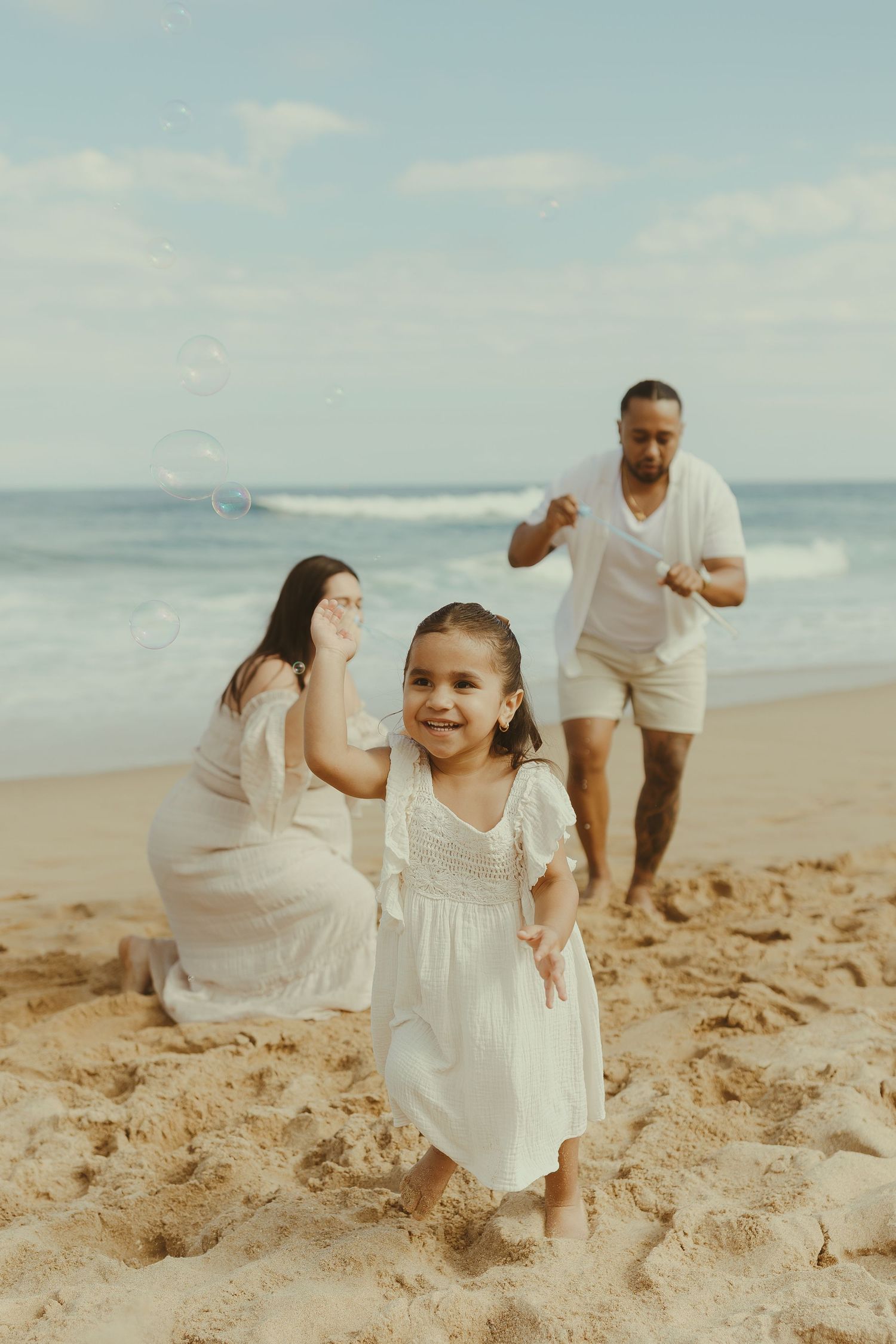 People dressed in white outfits run and laugh together on a sandy beach during a sunny day.