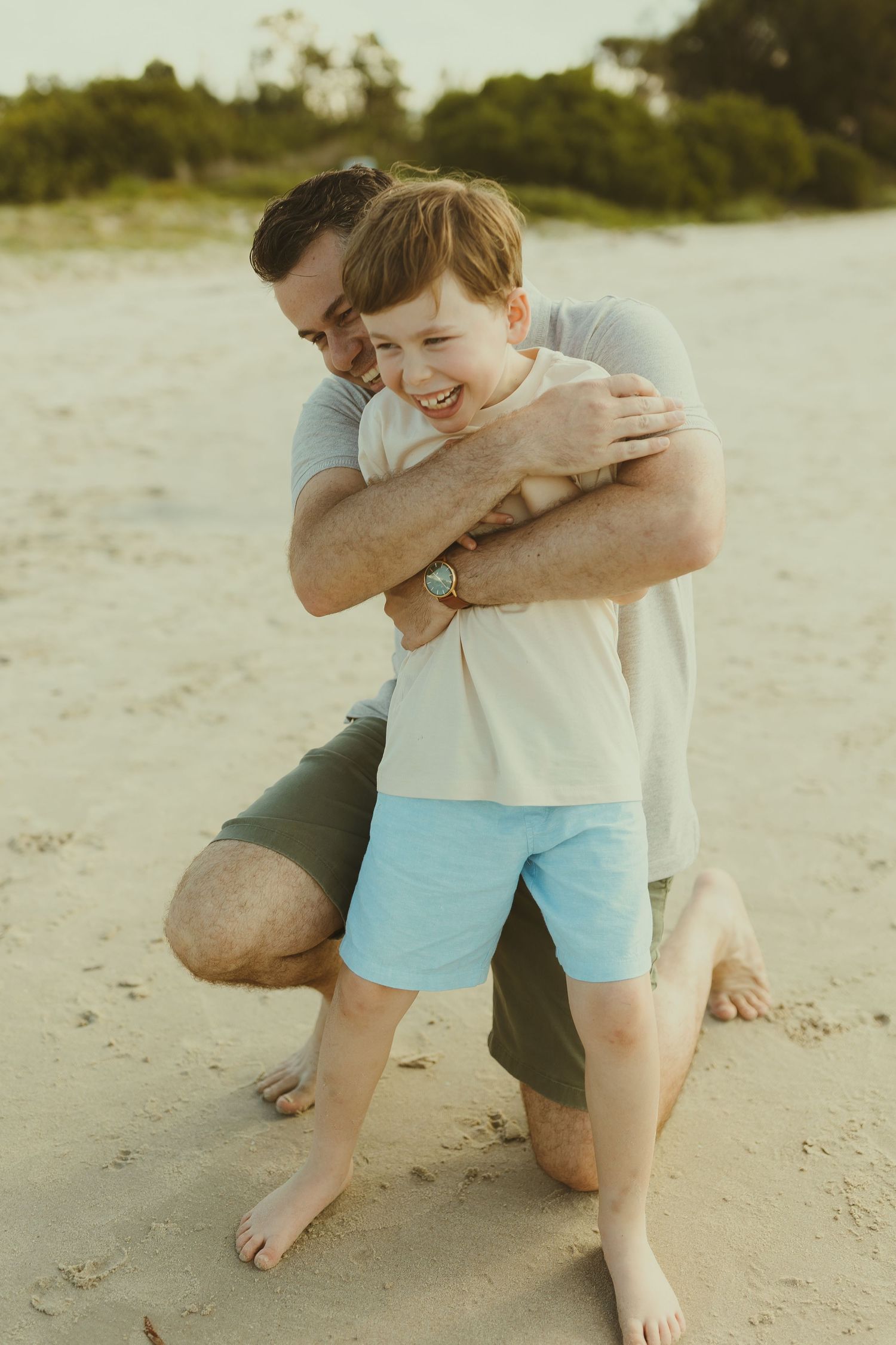 A joyful playtime moment between family members on a sandy beach.