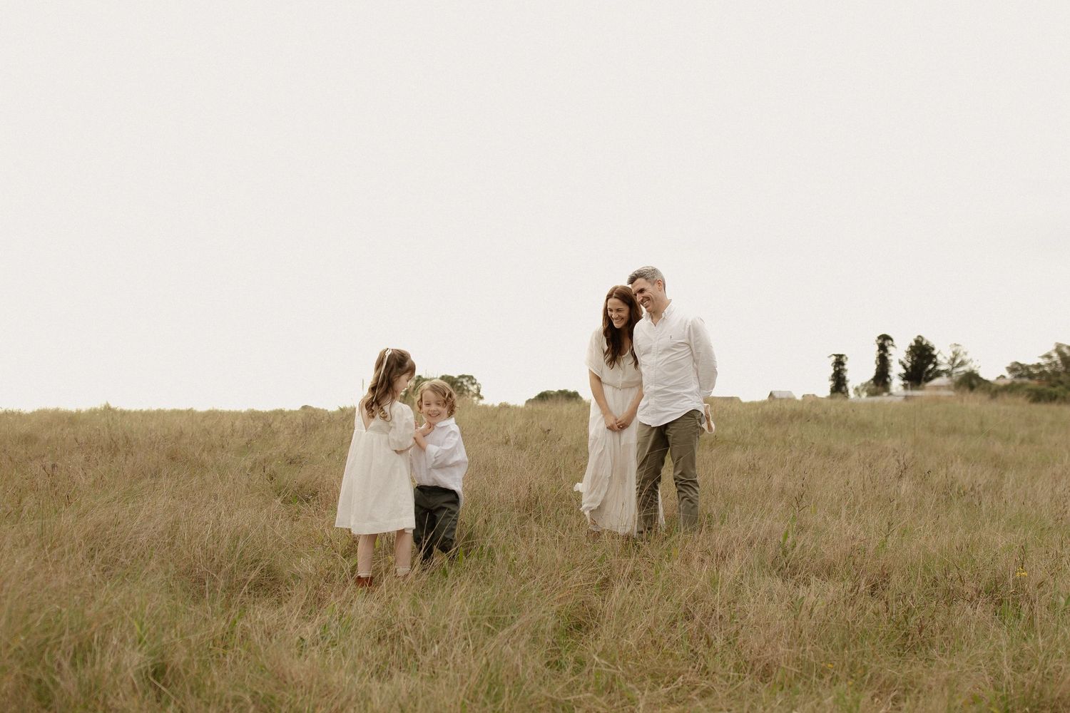 A group in white attire stands together on a grassy hill during sunset creating a dreamy silhouette.