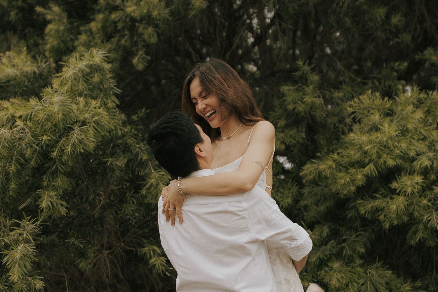 A person in a flowing white dress twirls gracefully in a lush green forest setting.