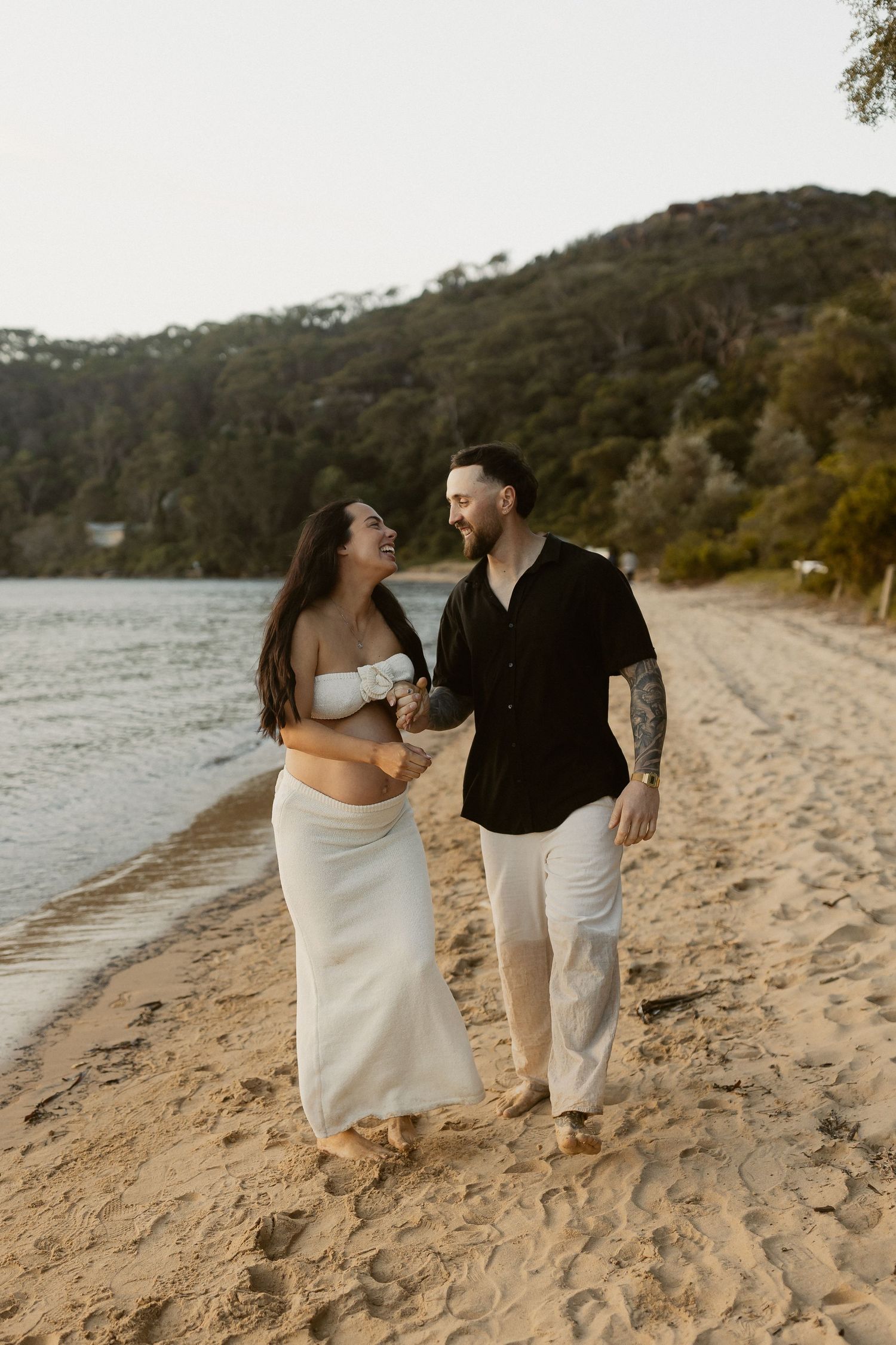 A couple shares romantic moments together walking along a sandy beach at sunset in Australia.