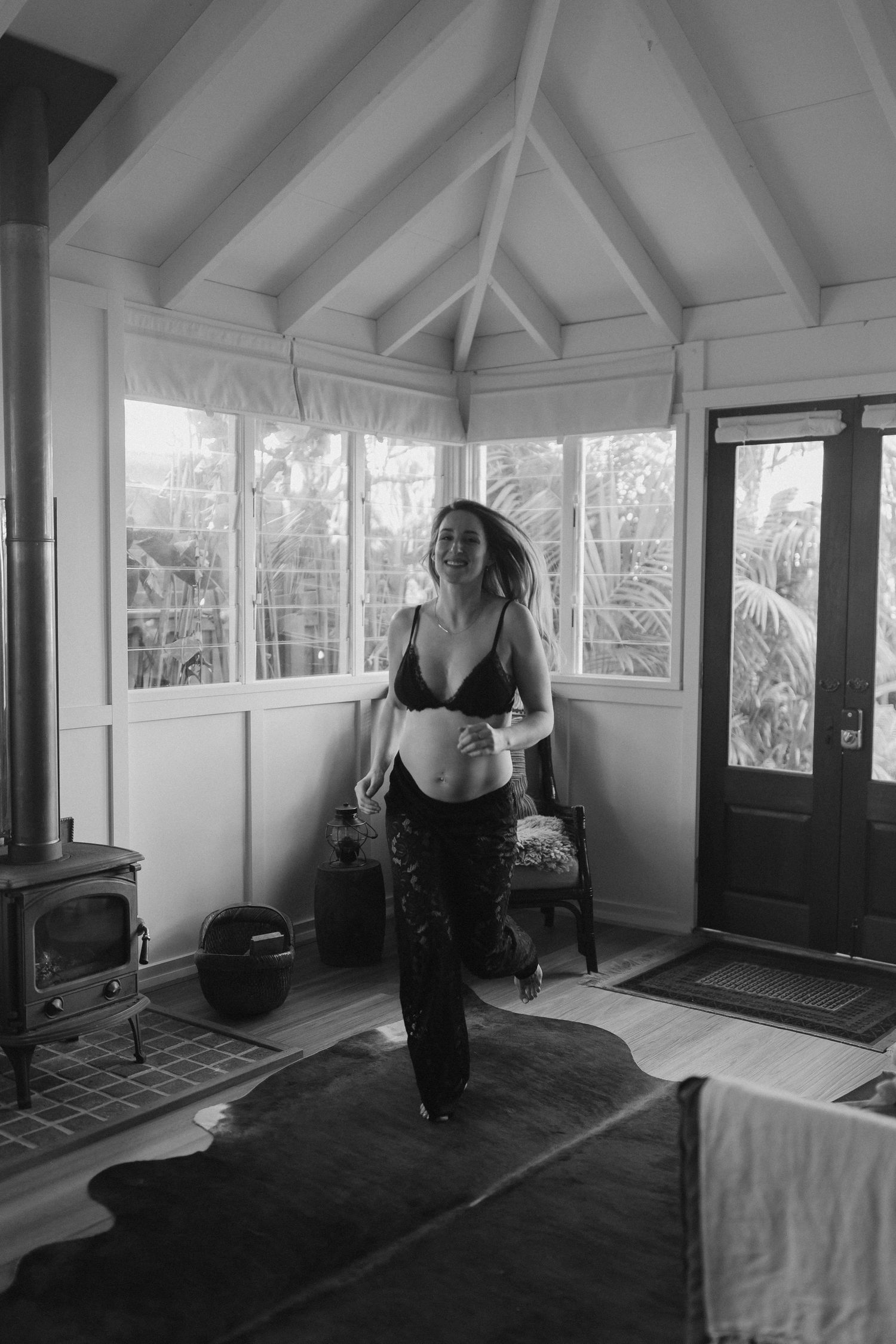 Monochrome maternity portrait in rustic room with vaulted ceiling and wood stove.