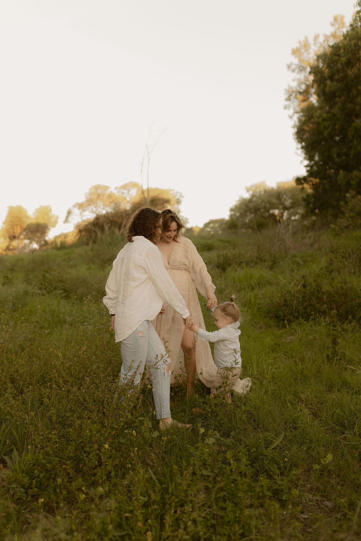 A family shares tender moments together in a sunlit meadow wearing light summer clothing.