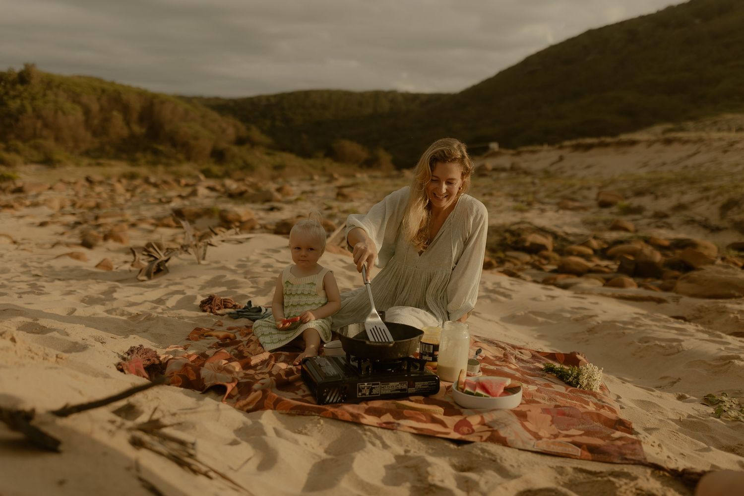 A scenic beach landscape with sand dunes and rocky cliffs under moody skies.