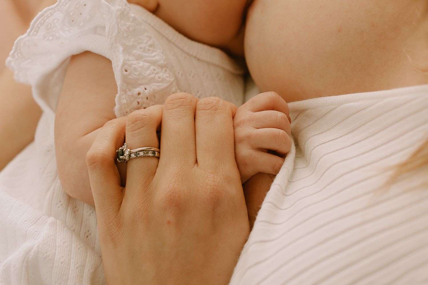 A delicate feminine hand with an engagement ring against white fabric.