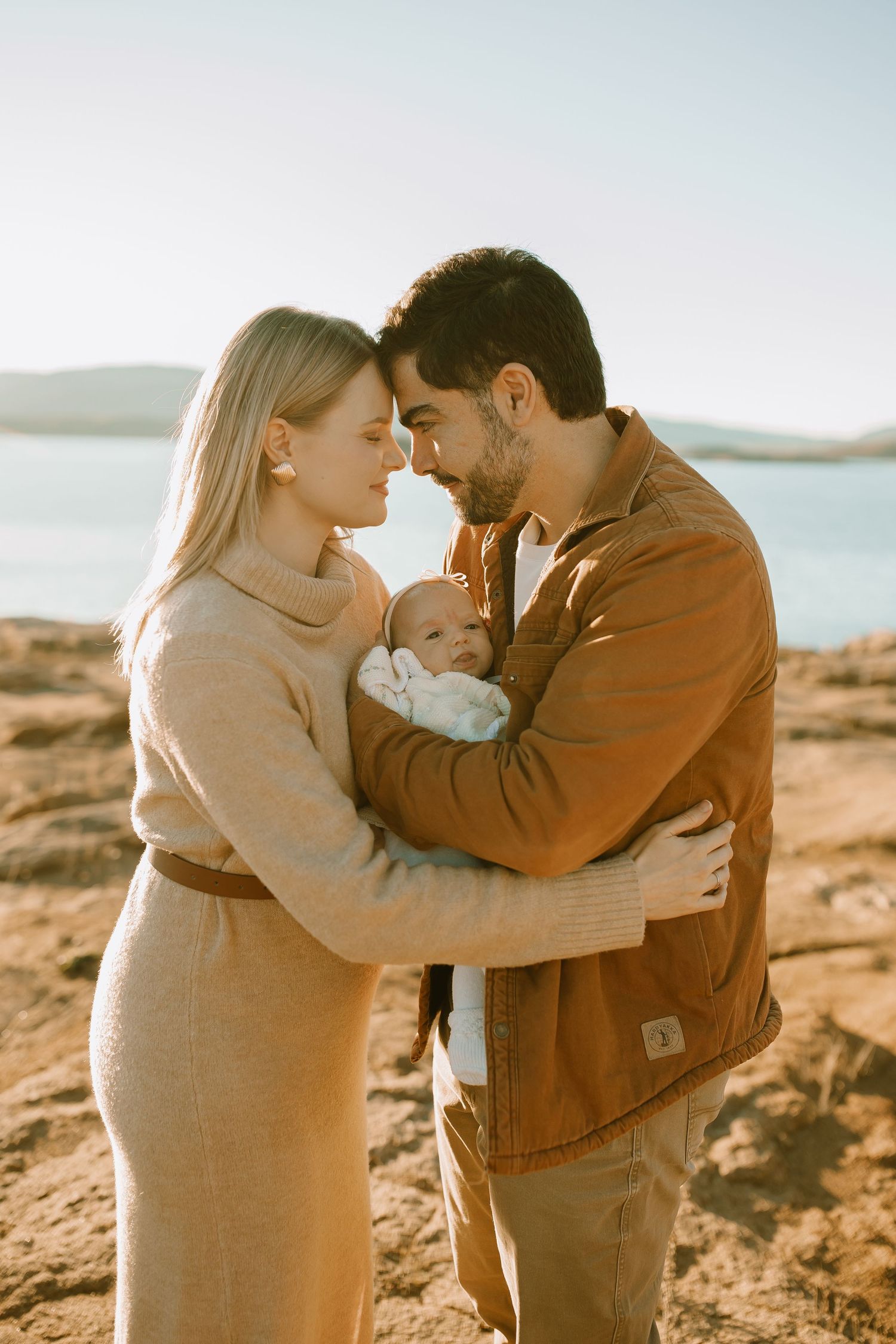 A family shares an intimate moment together on rocky shores with a serene lake in the background.