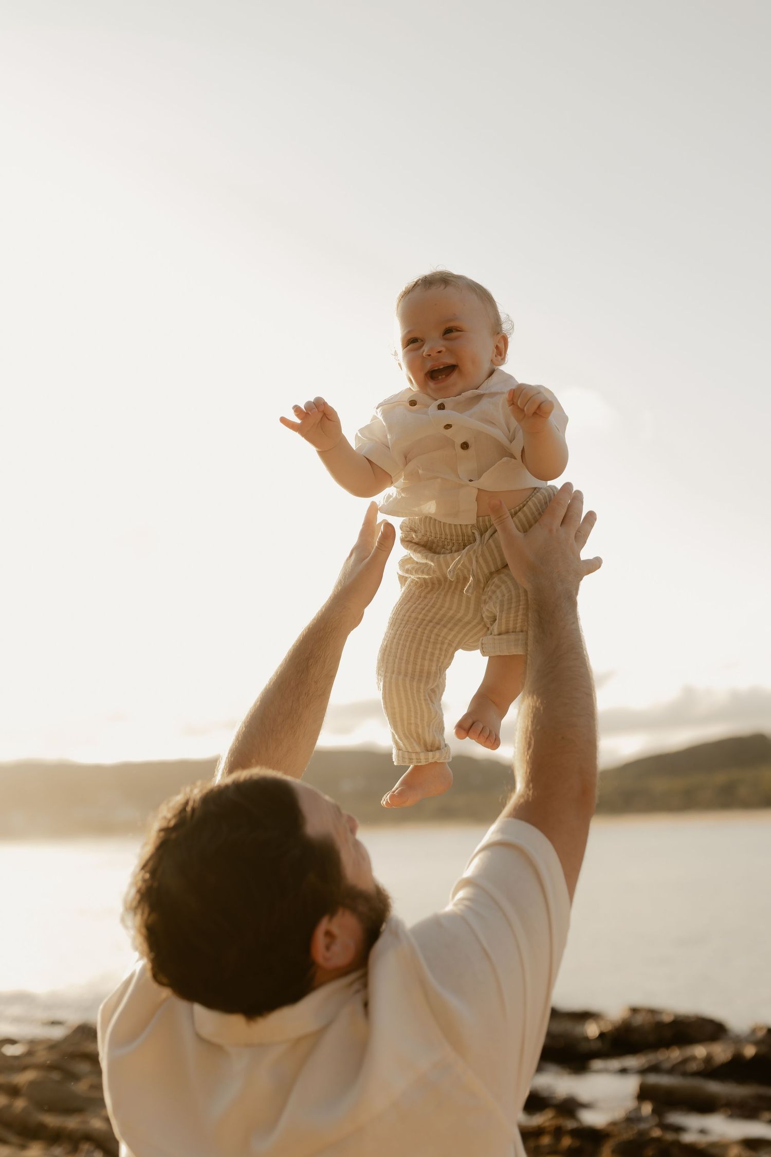 Parent lifts baby wearing knit sweater against sunset beach backdrop in three sequential photos.