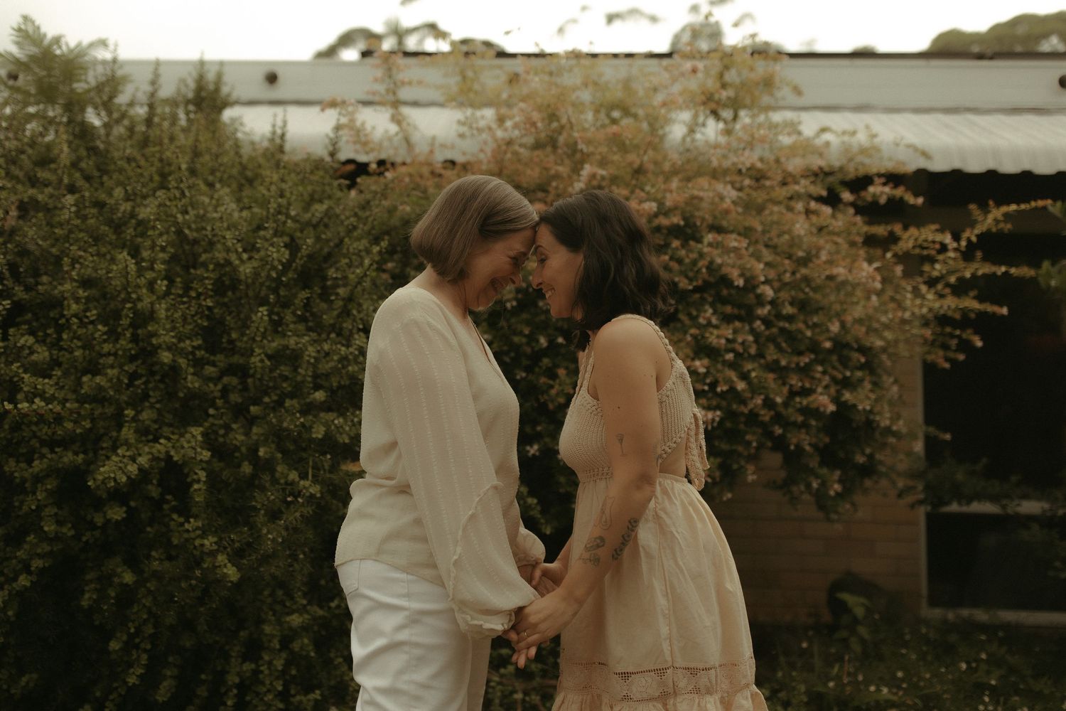 Two people share an intimate moment in a garden setting with golden evening light.
