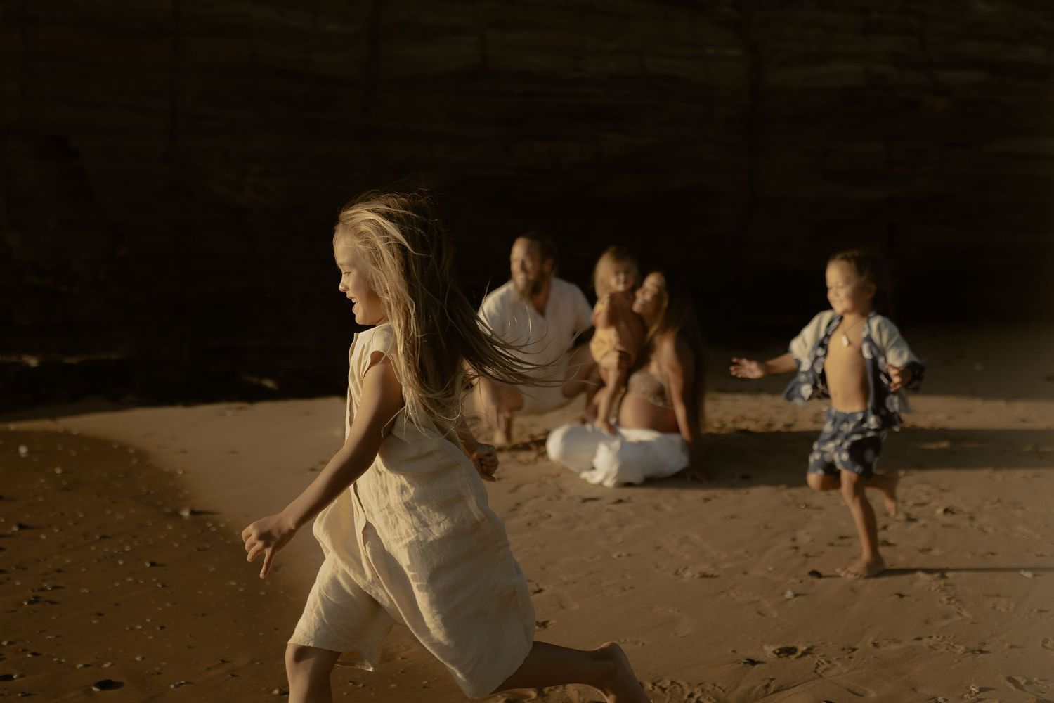 Family enjoying a sunset beach photoshoot with warm golden lighting and sandy backdrop.