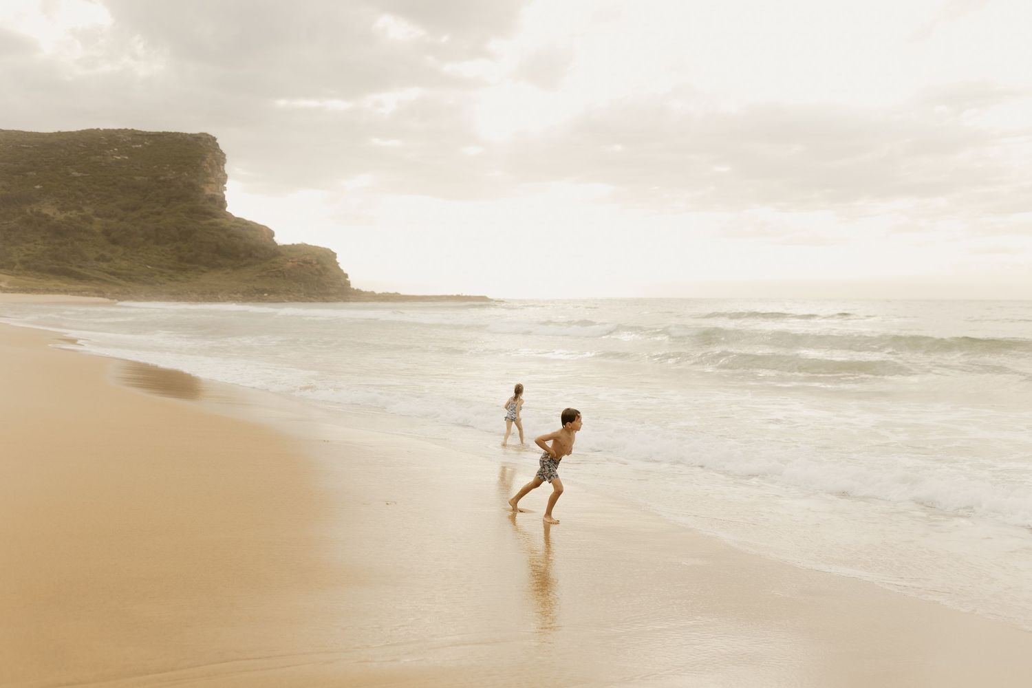 People walking along a misty beach at sunset with cliffs in the background.