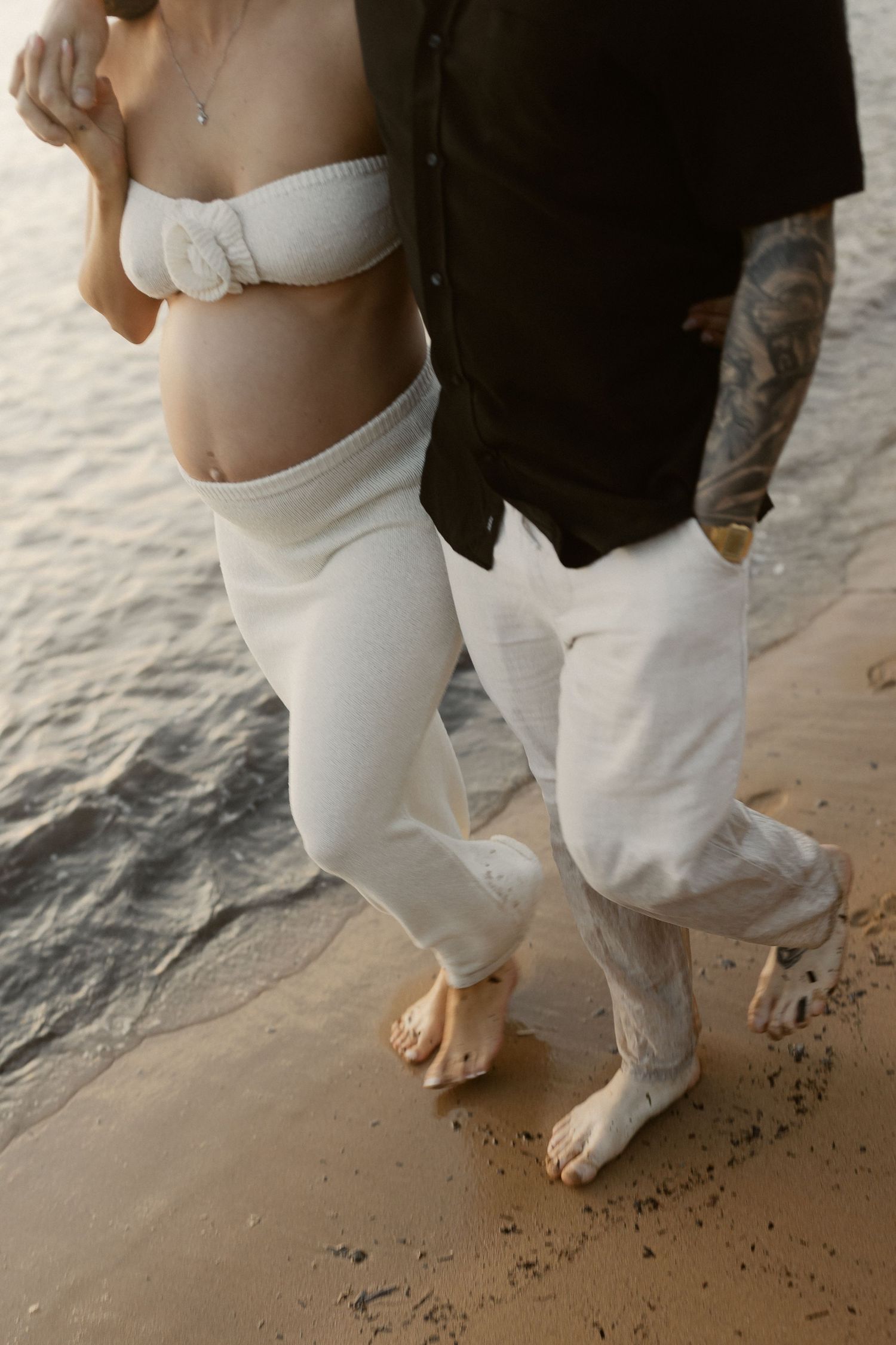 Bare feet walk together in the sand along the shoreline during a beach photoshoot.