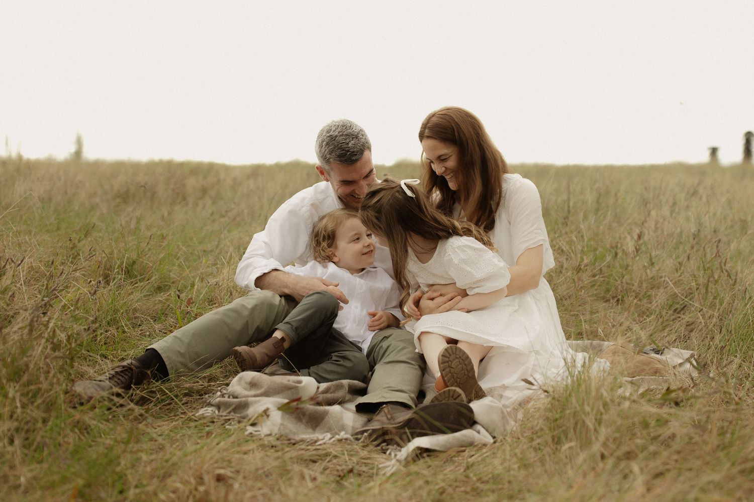 A romantic outdoor photo series showing tender moments between people sitting together in a golden grassy field.