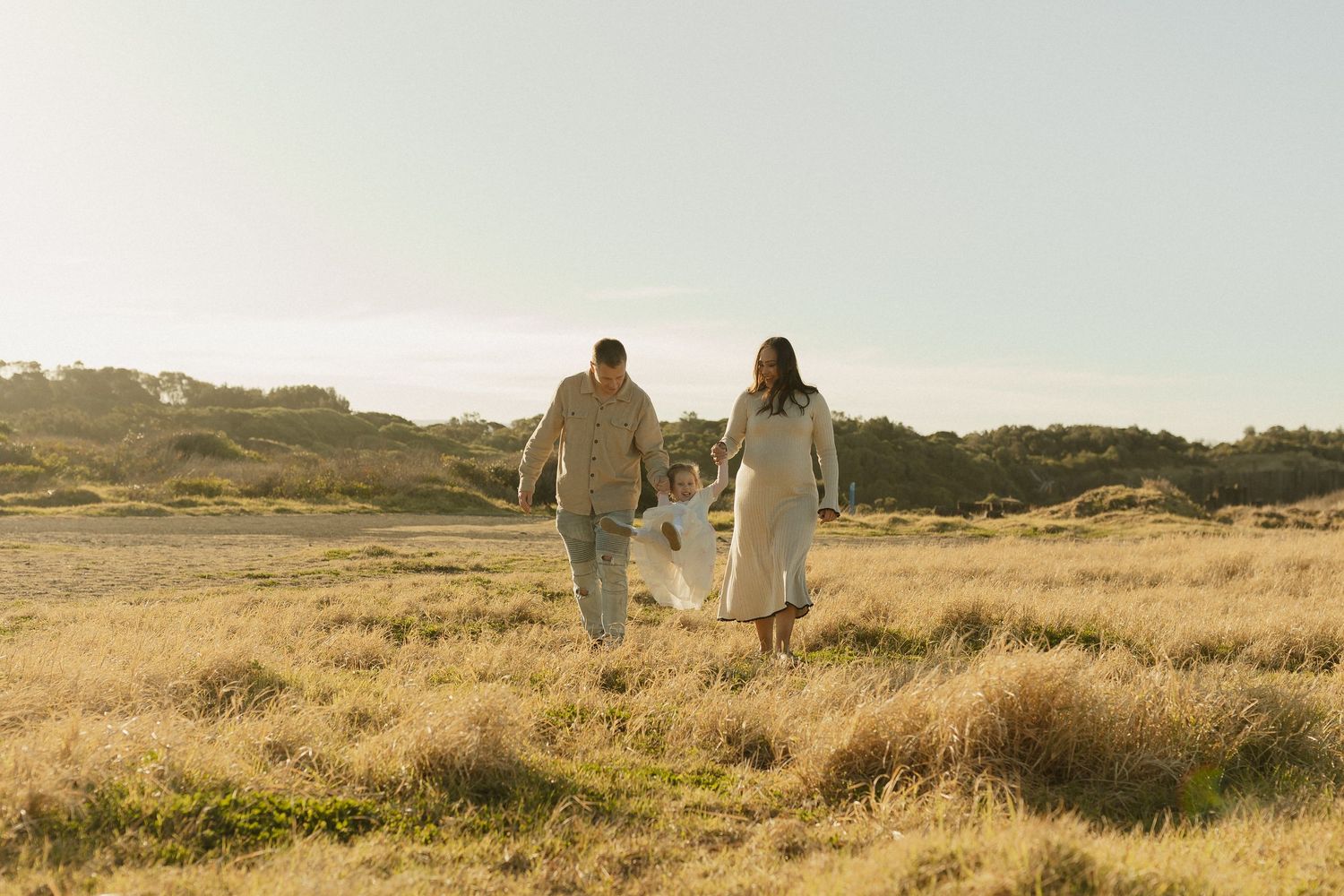 Couple walks hand in hand through golden grassland during sunset.