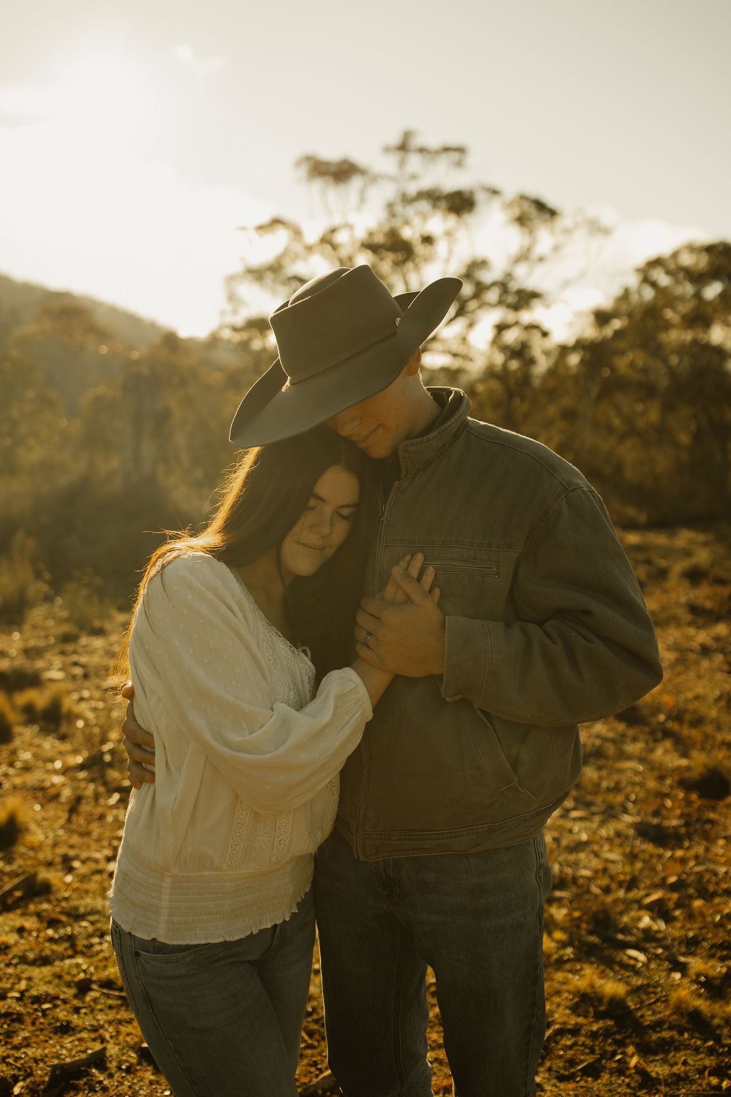 Two people share an intimate moment in cowboy attire against a golden sunset backdrop.