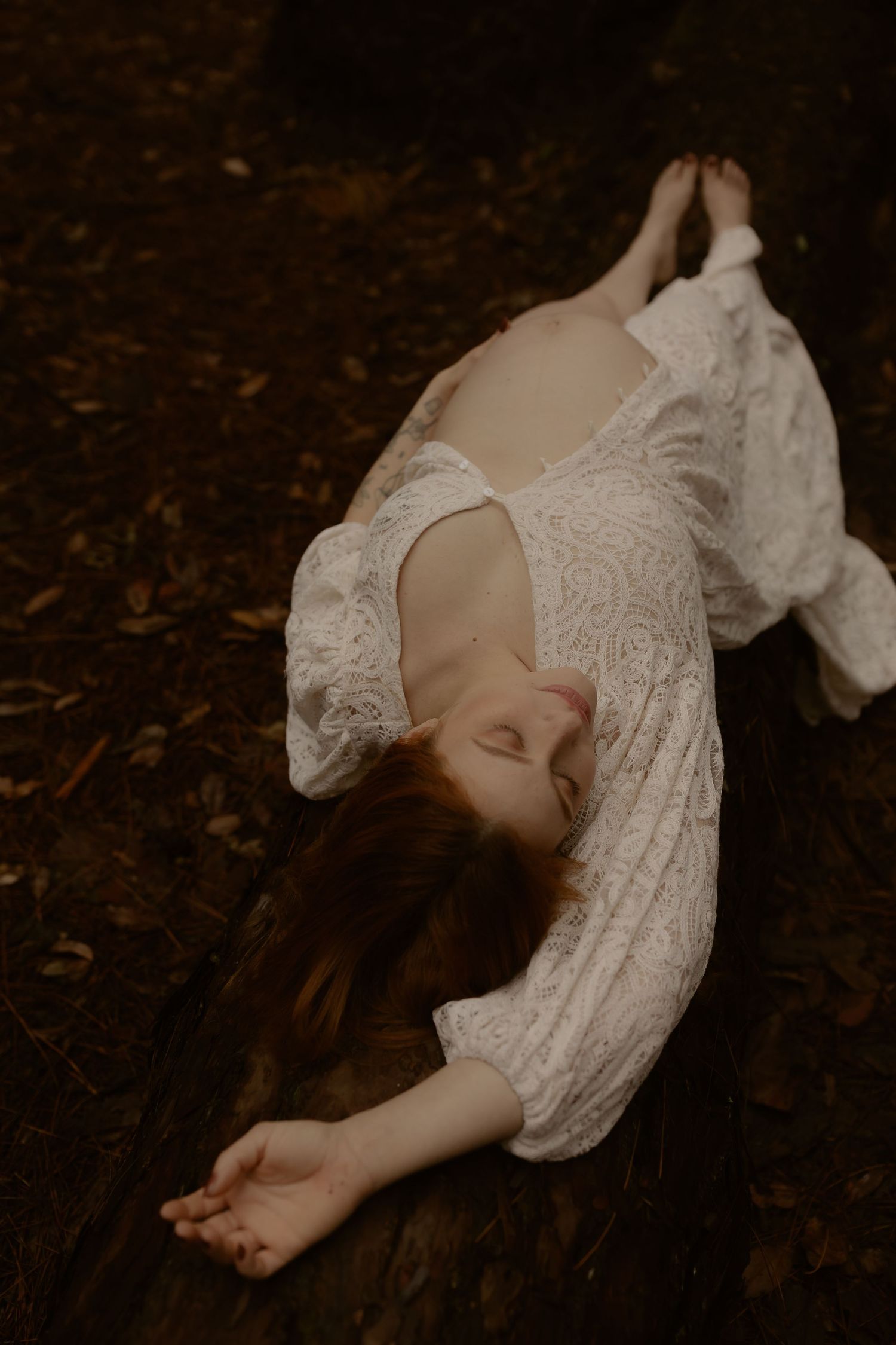Delicate white lace dress draped over reclining figure in moody forest setting.