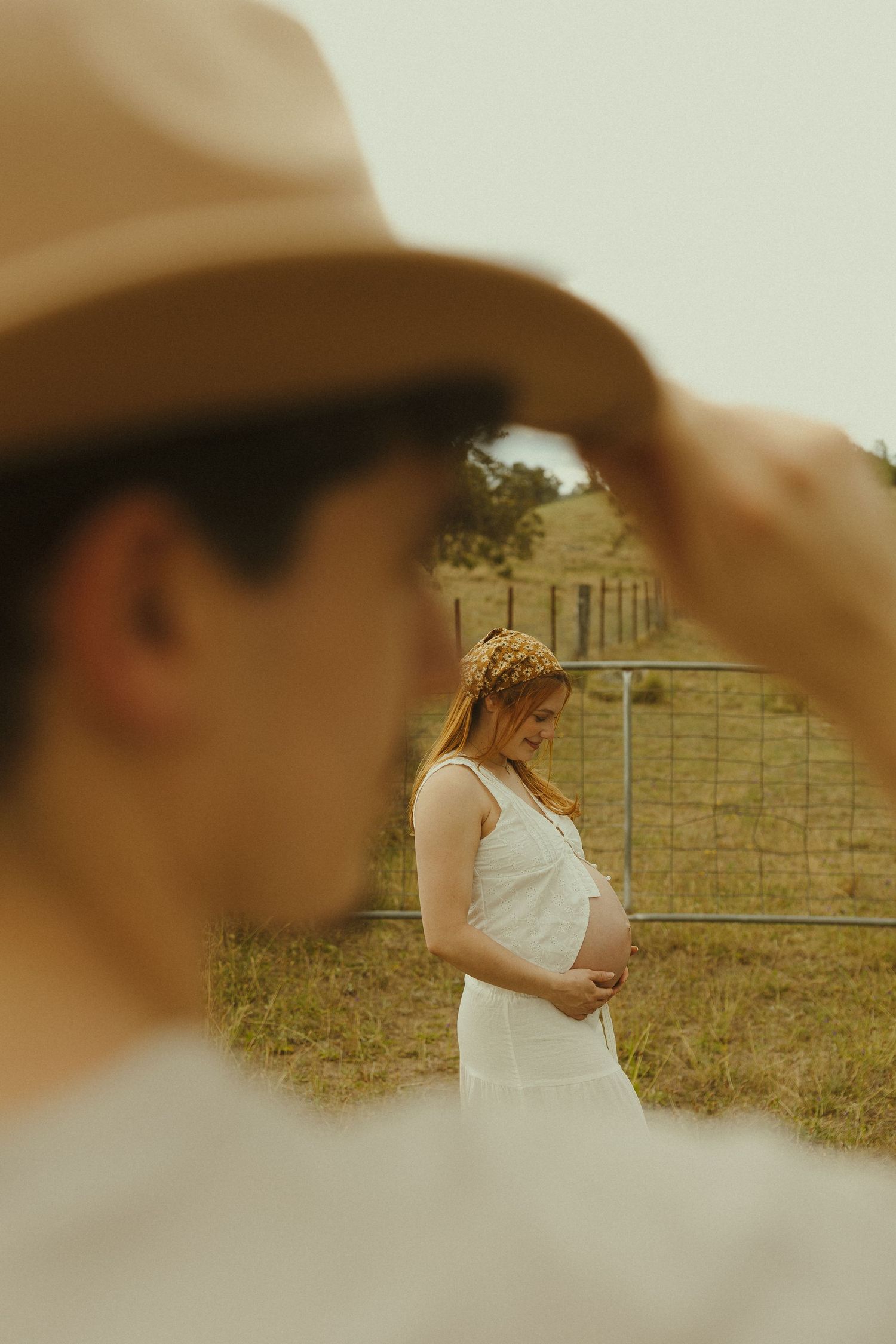 Artistic framed shot through a hat brim of figures in a rustic countryside setting.