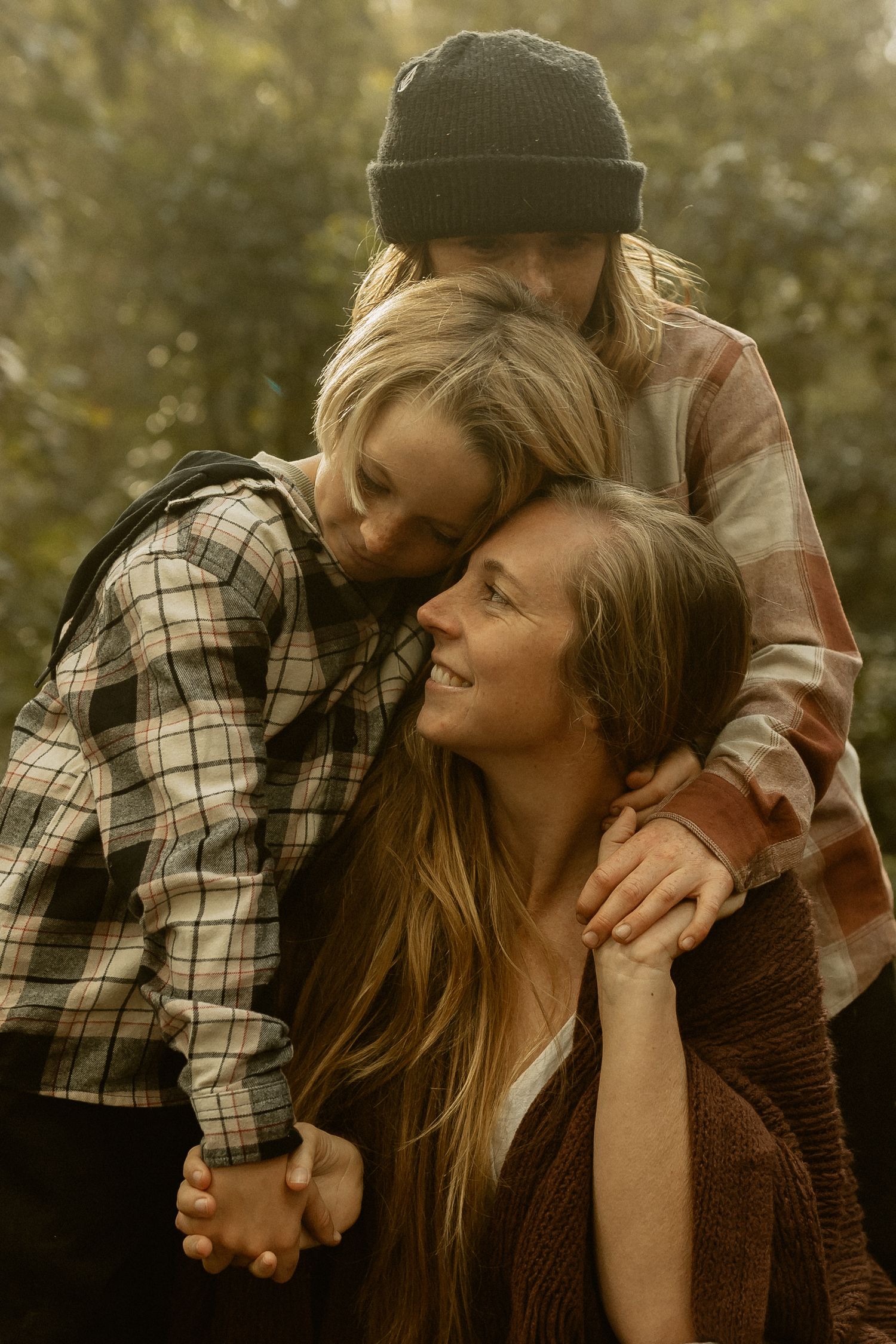 Three people in warm fall clothing share an intimate moment outdoors with natural lighting and warm tones.