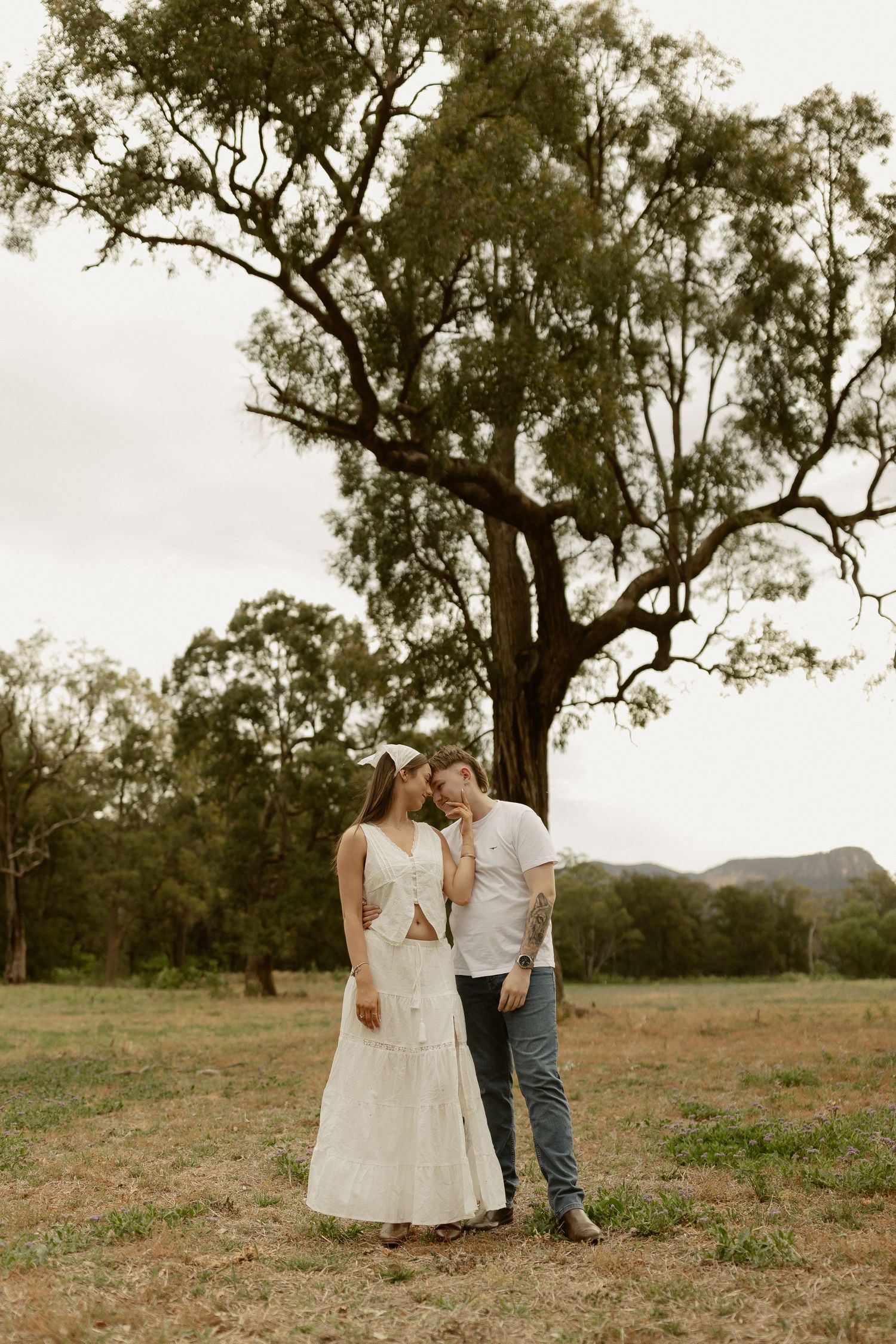A tender moment shared beneath a large gum tree in the Australian countryside.