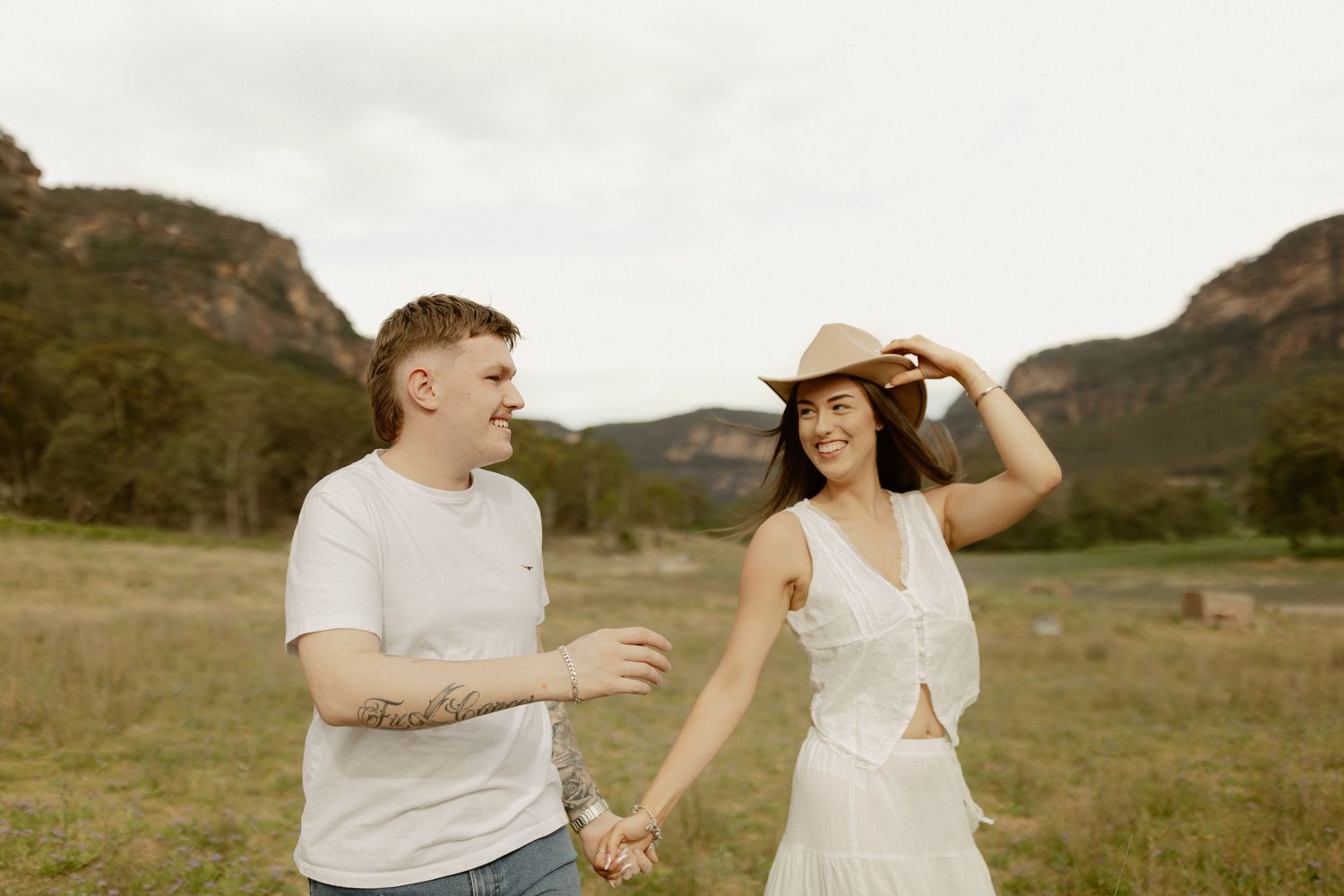 A couple shares joyful moments together in a scenic mountain meadow during a golden hour photoshoot.