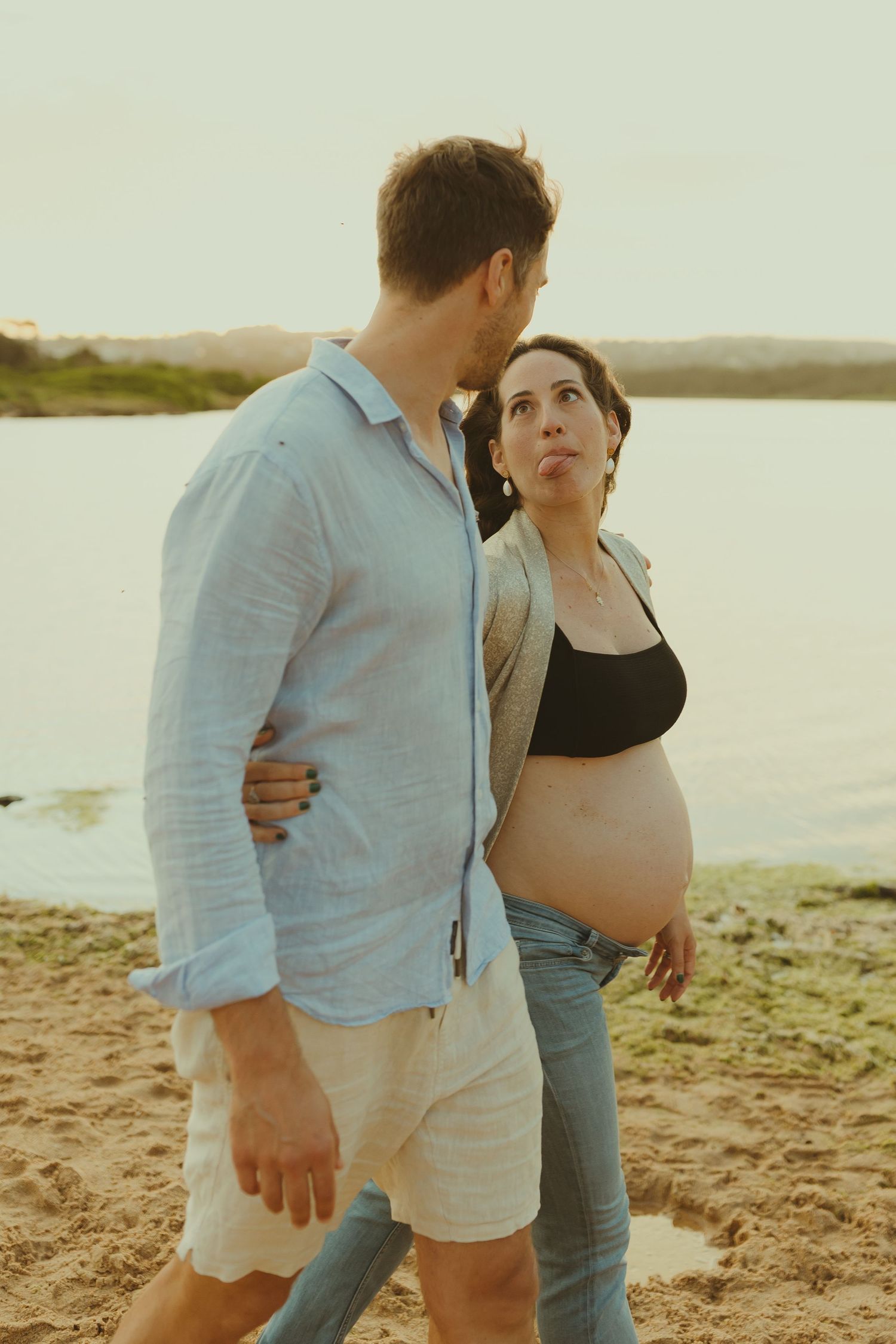Couple walking together on a sandy beach at sunset wearing light blue and black clothing.