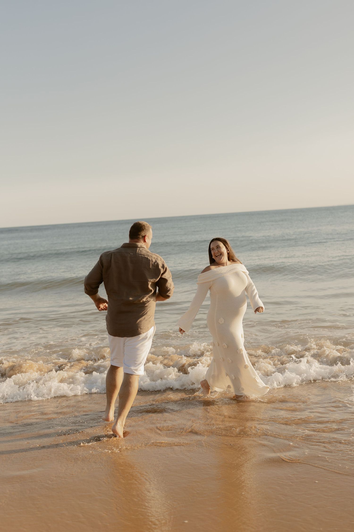 People playing and splashing in ocean waves at the beach during golden hour.