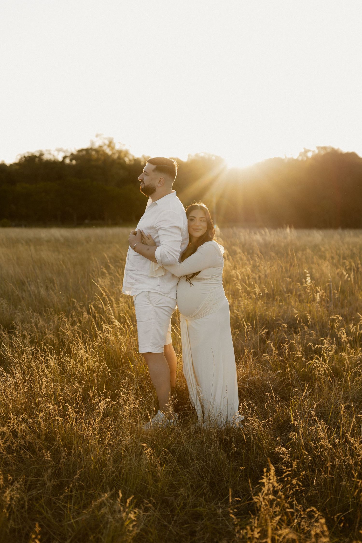A couple embraces in a golden sunlit field during sunset creating a romantic silhouette against the warm sky.