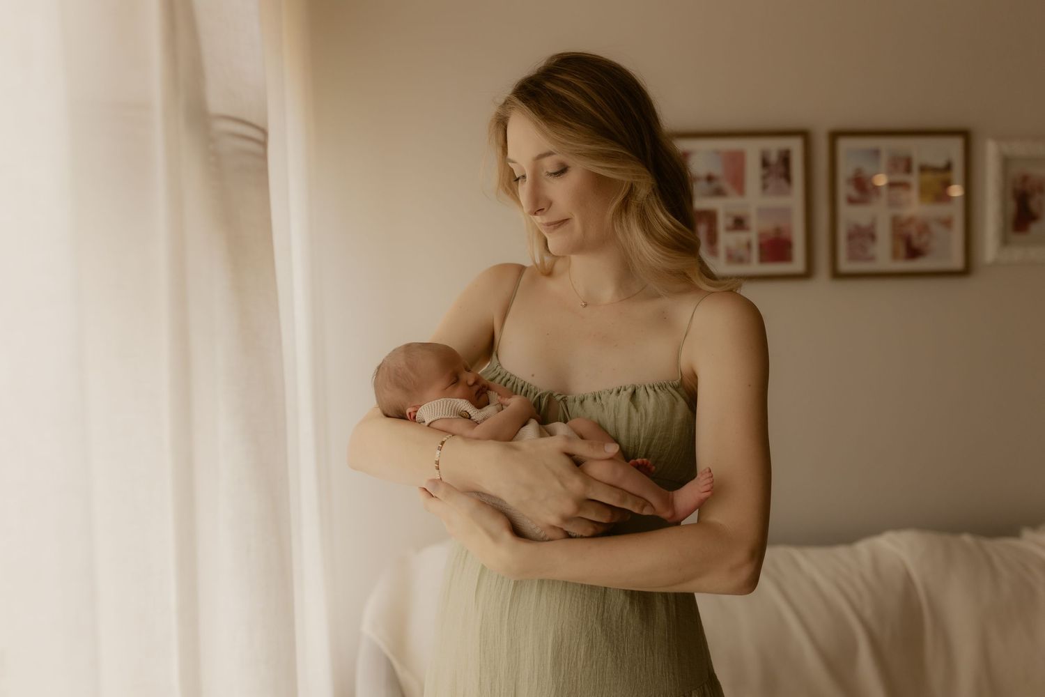 Tender moment captured in soft light as a newborn is cradled in a sage green dress.