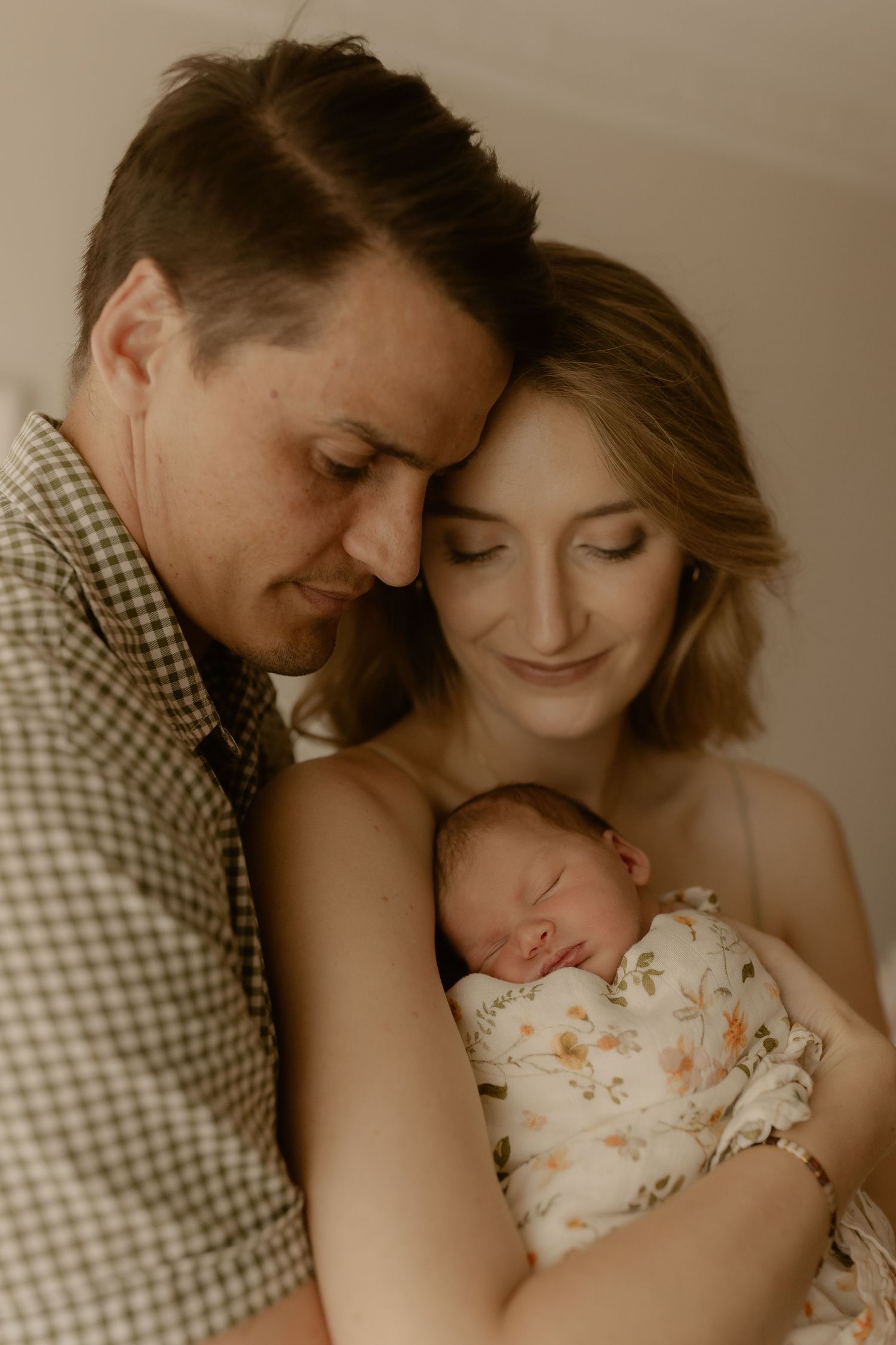 Intimate family moment with parents cradling their newborn baby in warm sepia tones.
